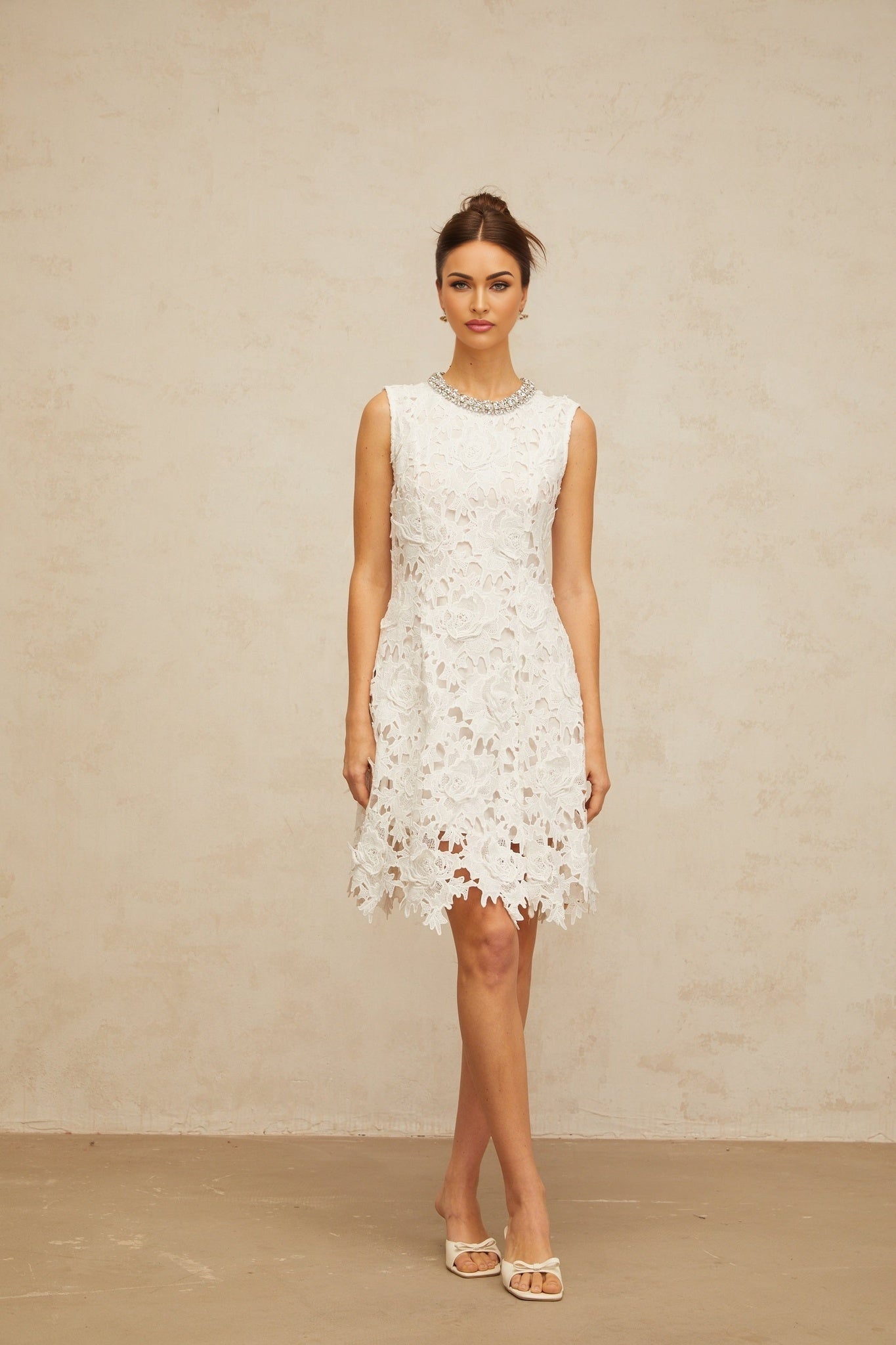 A white mini dress with corded lace detailing and embellishments on a mannequin or model against a plain background