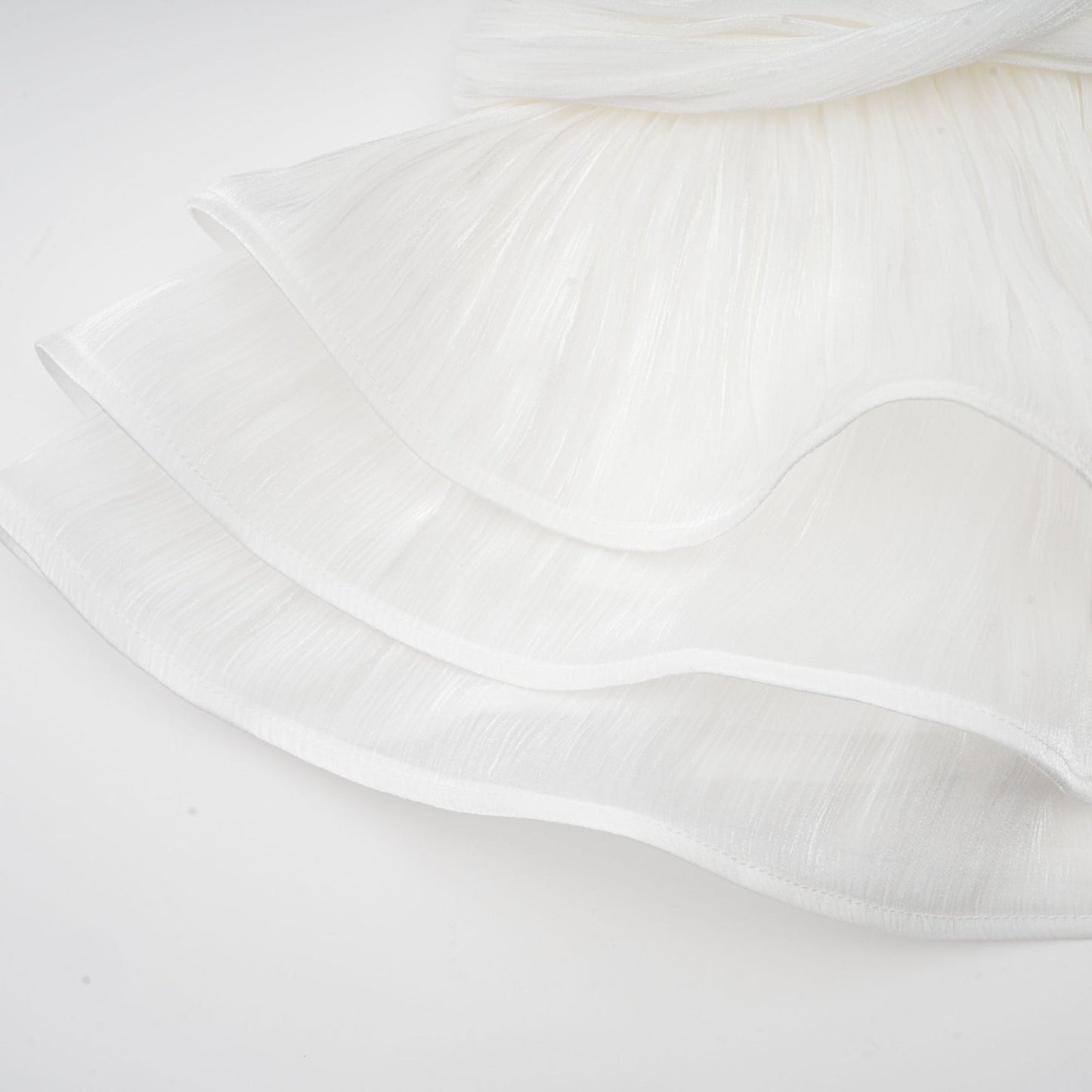 A white mini dress with full pleats and a cinched waist featuring a rosier design on a model against a plain background