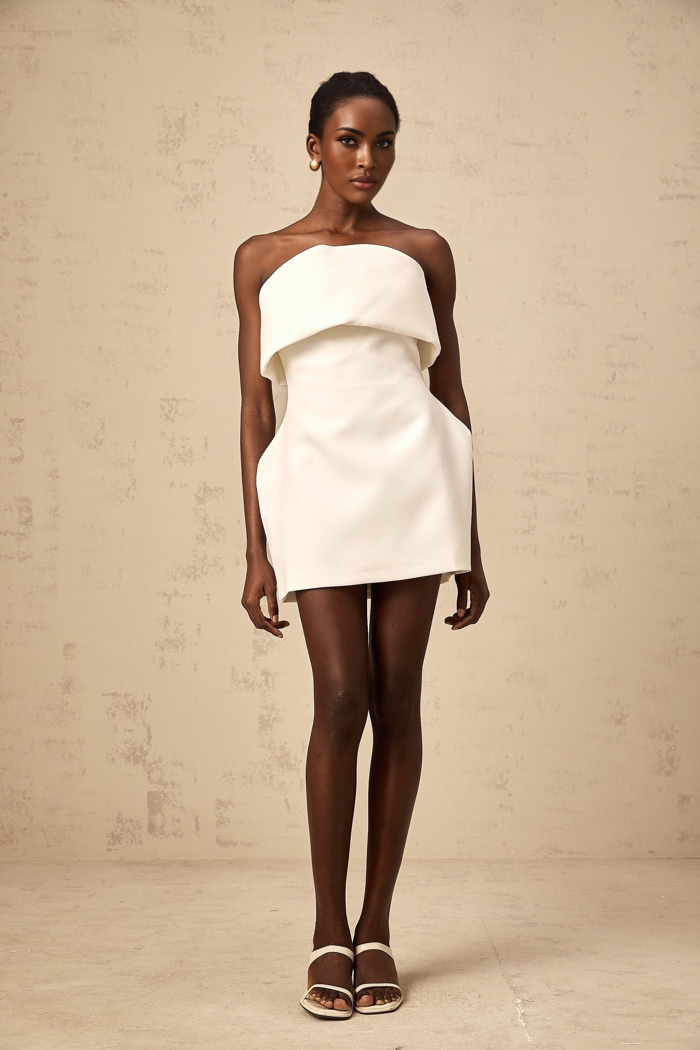 A white mini dress with offshoulder neckline and puff sleeves worn by a model against a plain background
