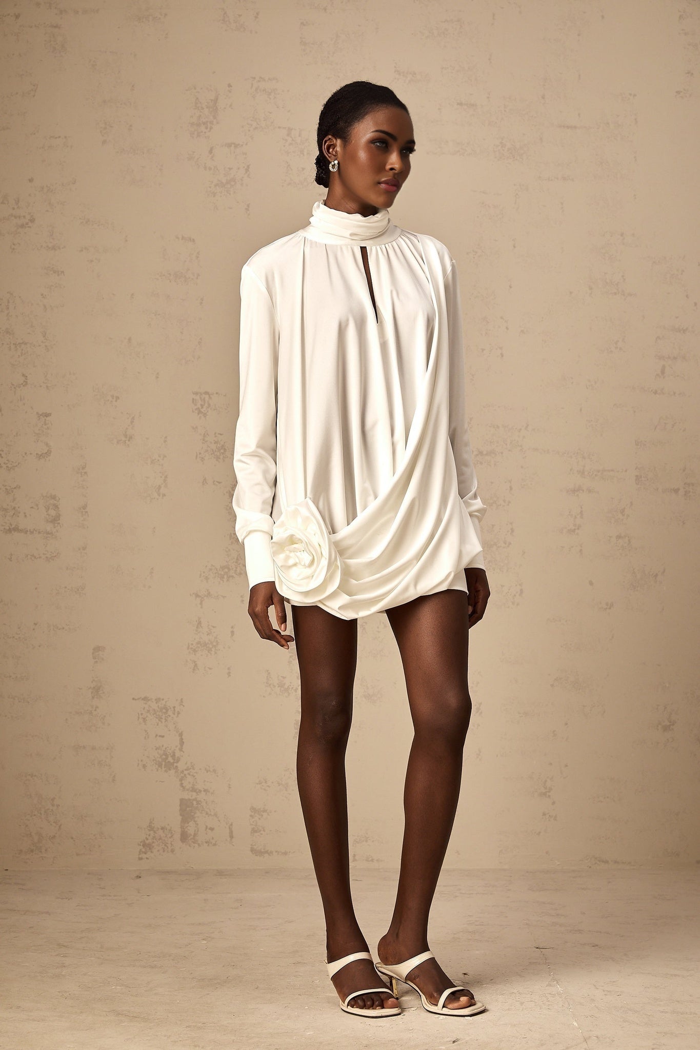 A white mini dress with ruched detailing and faux flower embellishments featuring a fitted silhouette and short length