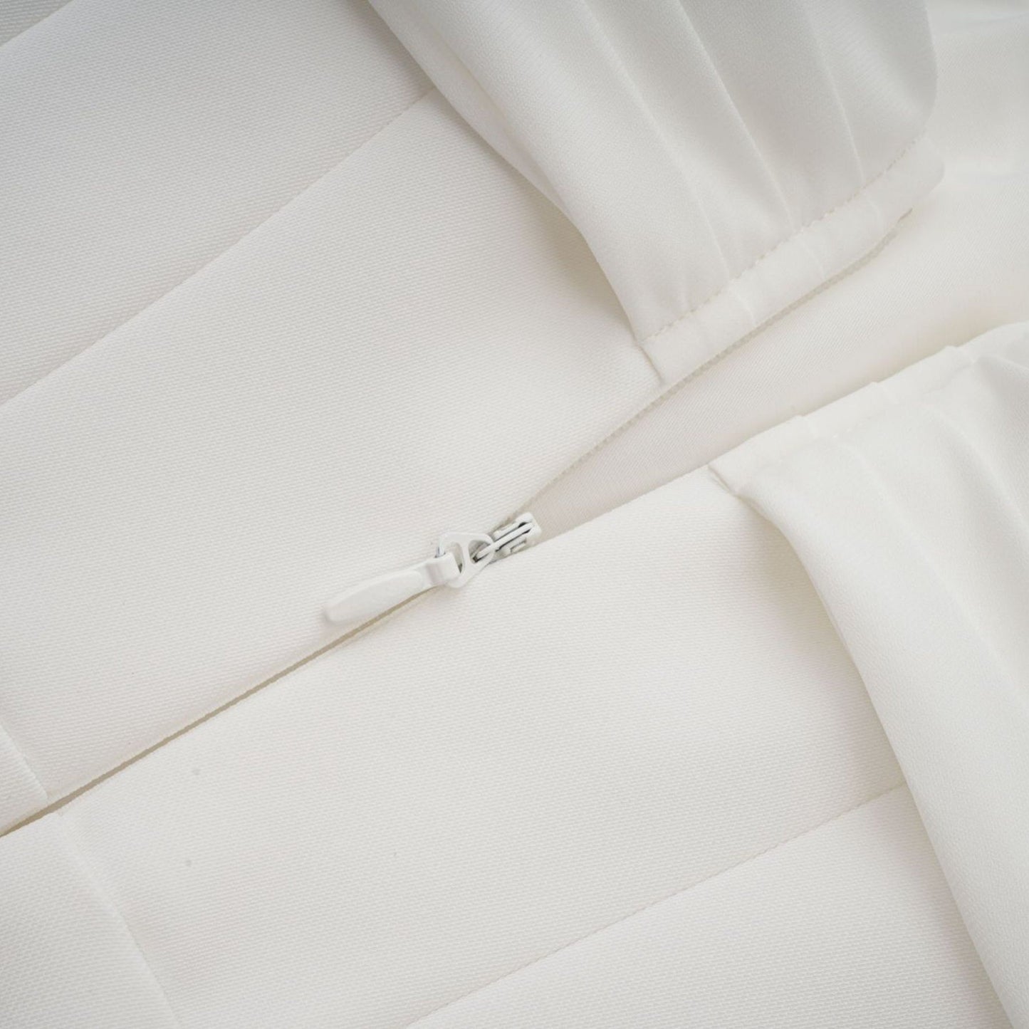 A white mini dress with ruched fabric and ribbon design details worn by a model against a plain background