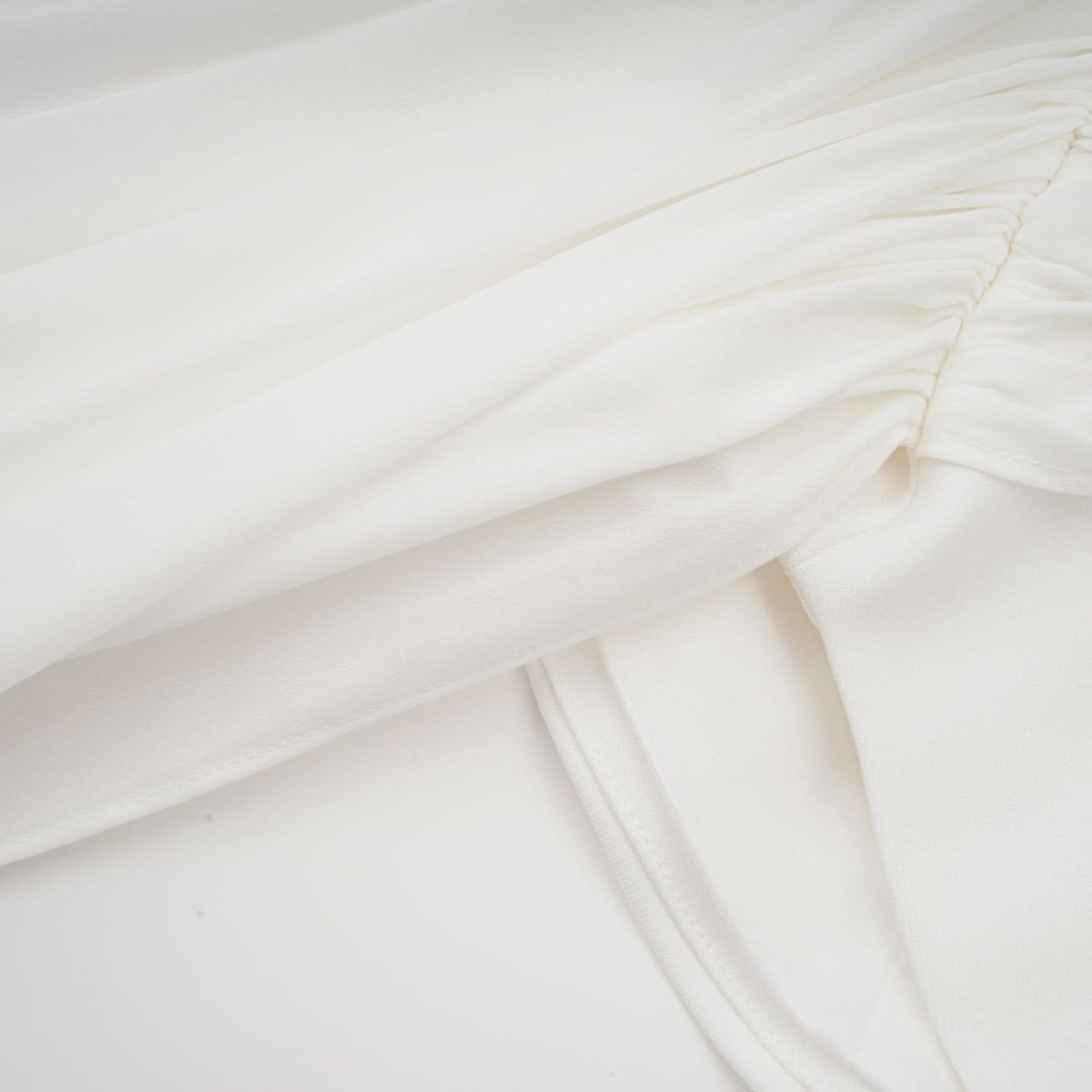 A white mini dress with ruched fabric and ribbon design details worn by a model against a plain background