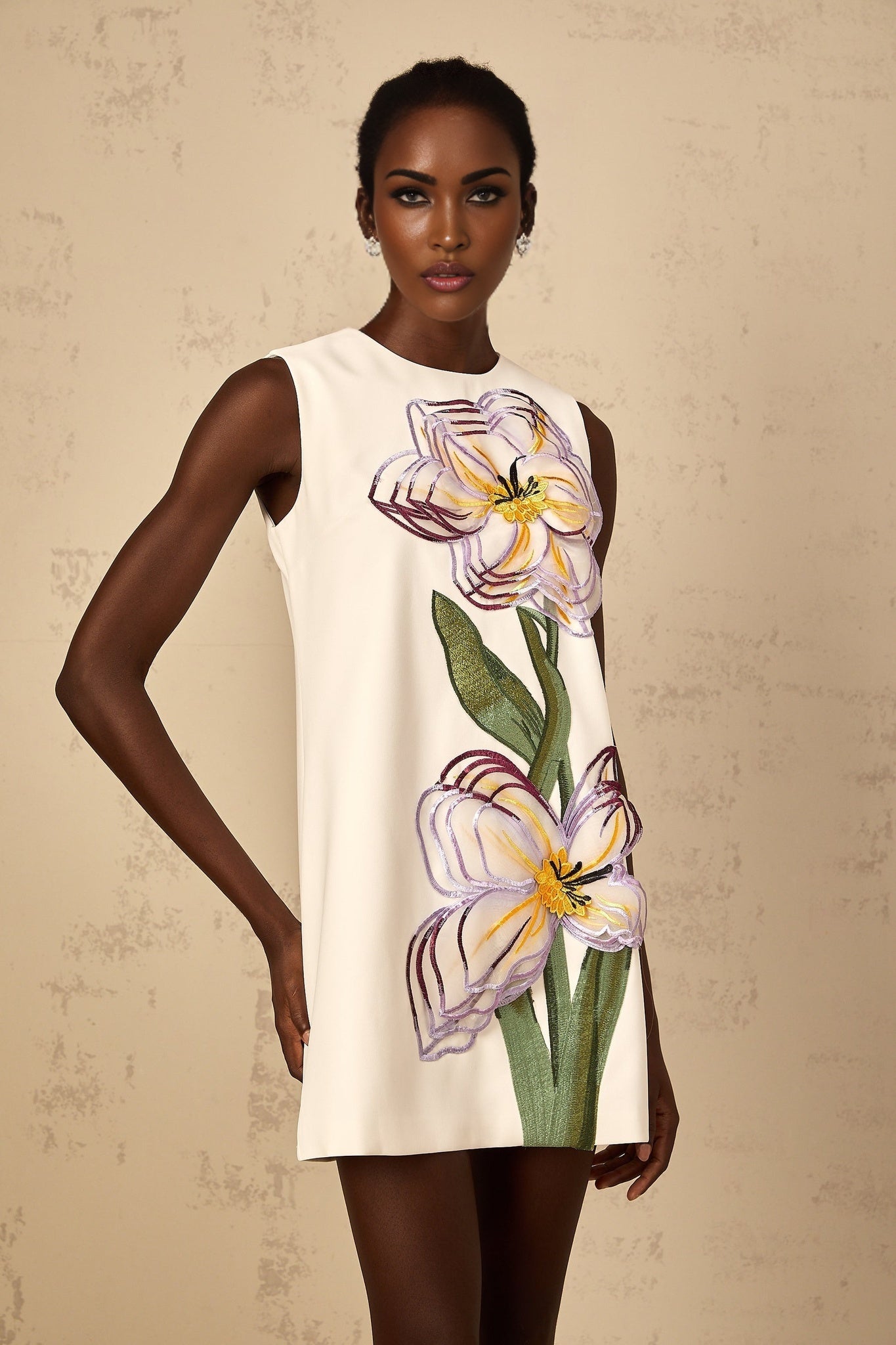 A white mini dress with sequin and floral embroidery details worn by a female model standing against a plain background
