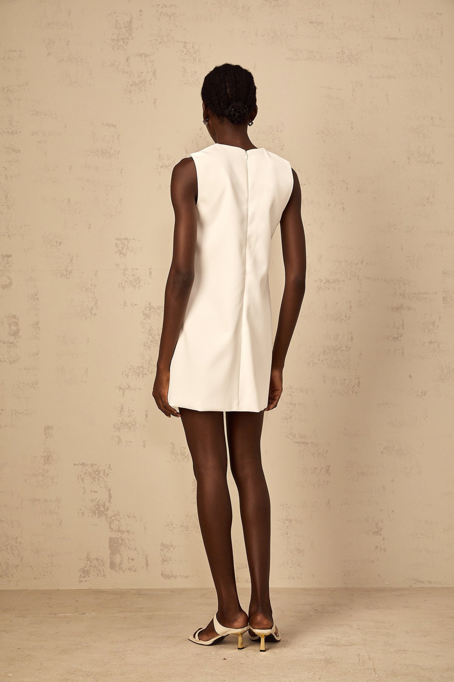 A white mini dress with sequin floral embroidery worn by a woman standing in a relaxed pose