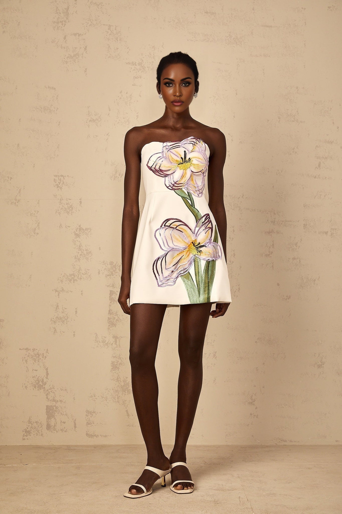 A white off shoulder mini dress with sequin and floral embroidery details worn by a woman named Irene
