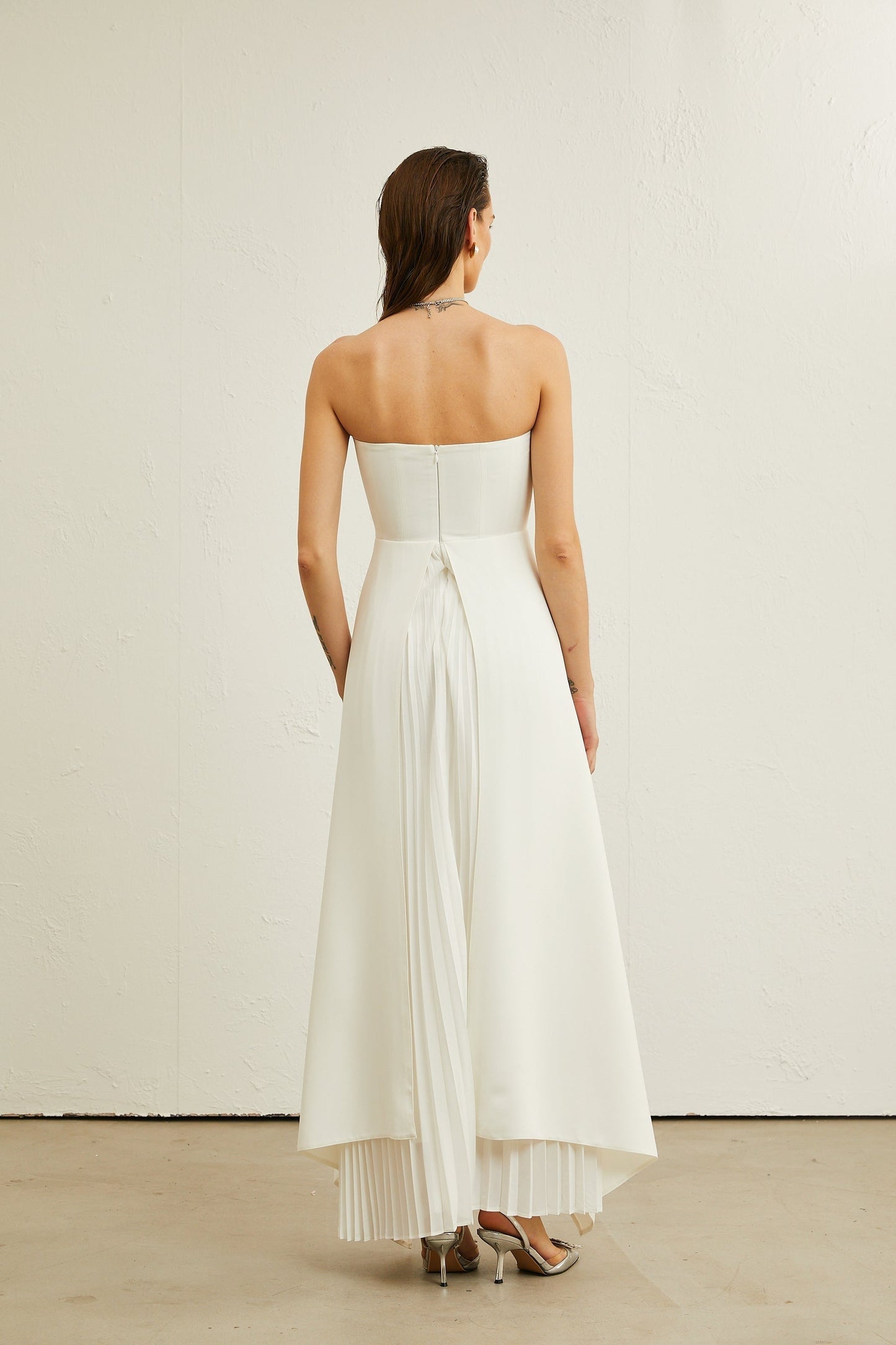 A white offshoulder maxi dress with pleated details worn by a model named Vanessa