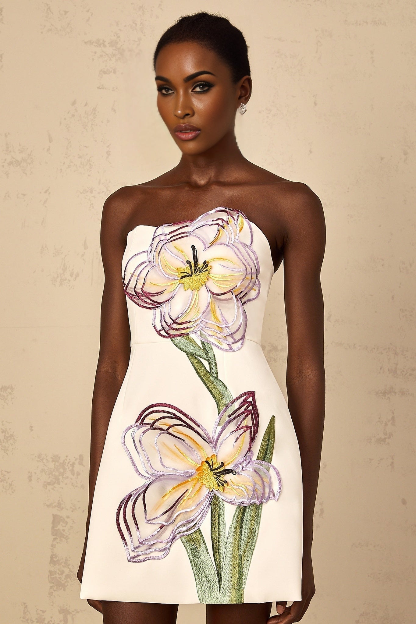 A white offshoulder mini dress with sequin floral embroidery worn by a woman against a plain background