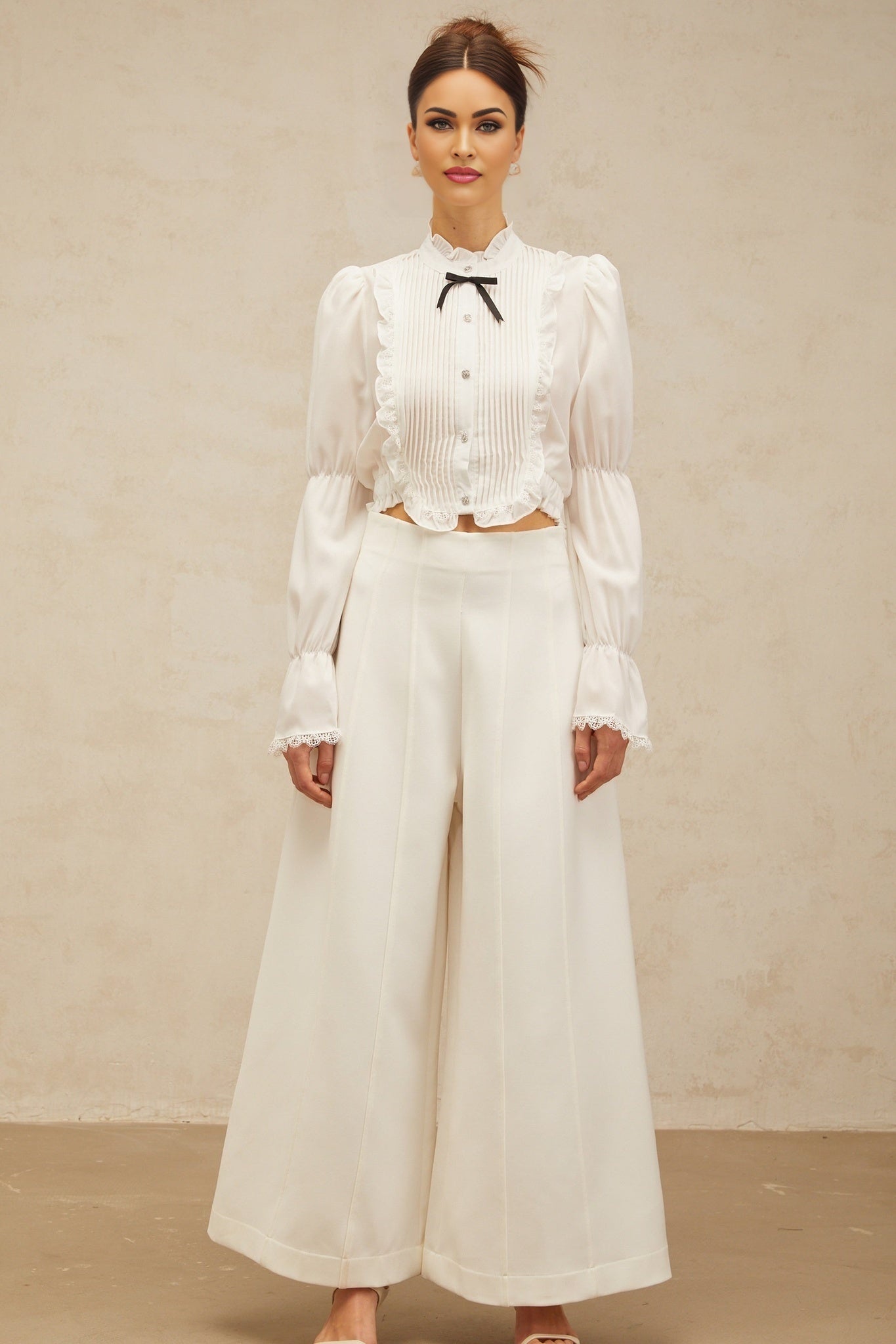 A white ruffled shirt with a bow tie neckline and shirred panels featuring a feminine and elegant design
