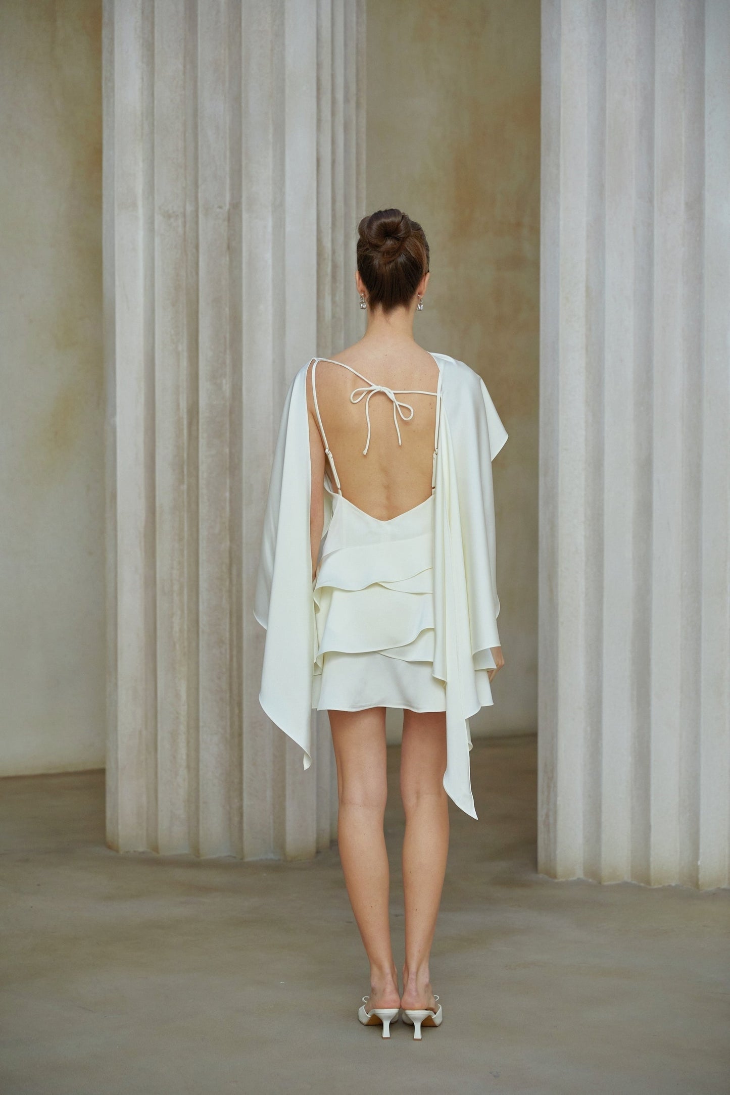 A white satin mini dress with ruffle details and a shawl panel featuring a fitted silhouette and short length