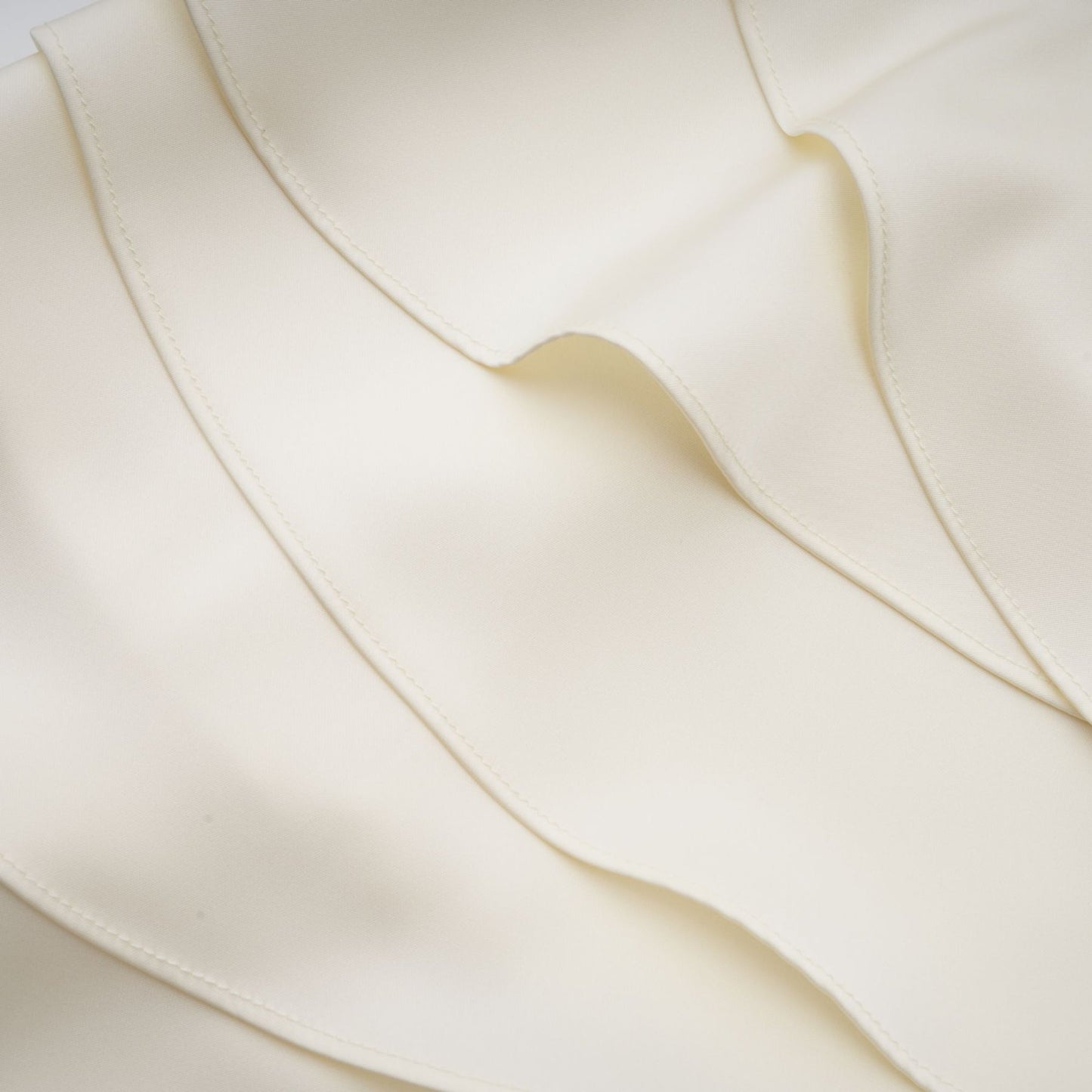 A white satin mini dress with ruffled details and a shawl panel accessory worn by a model against a plain background