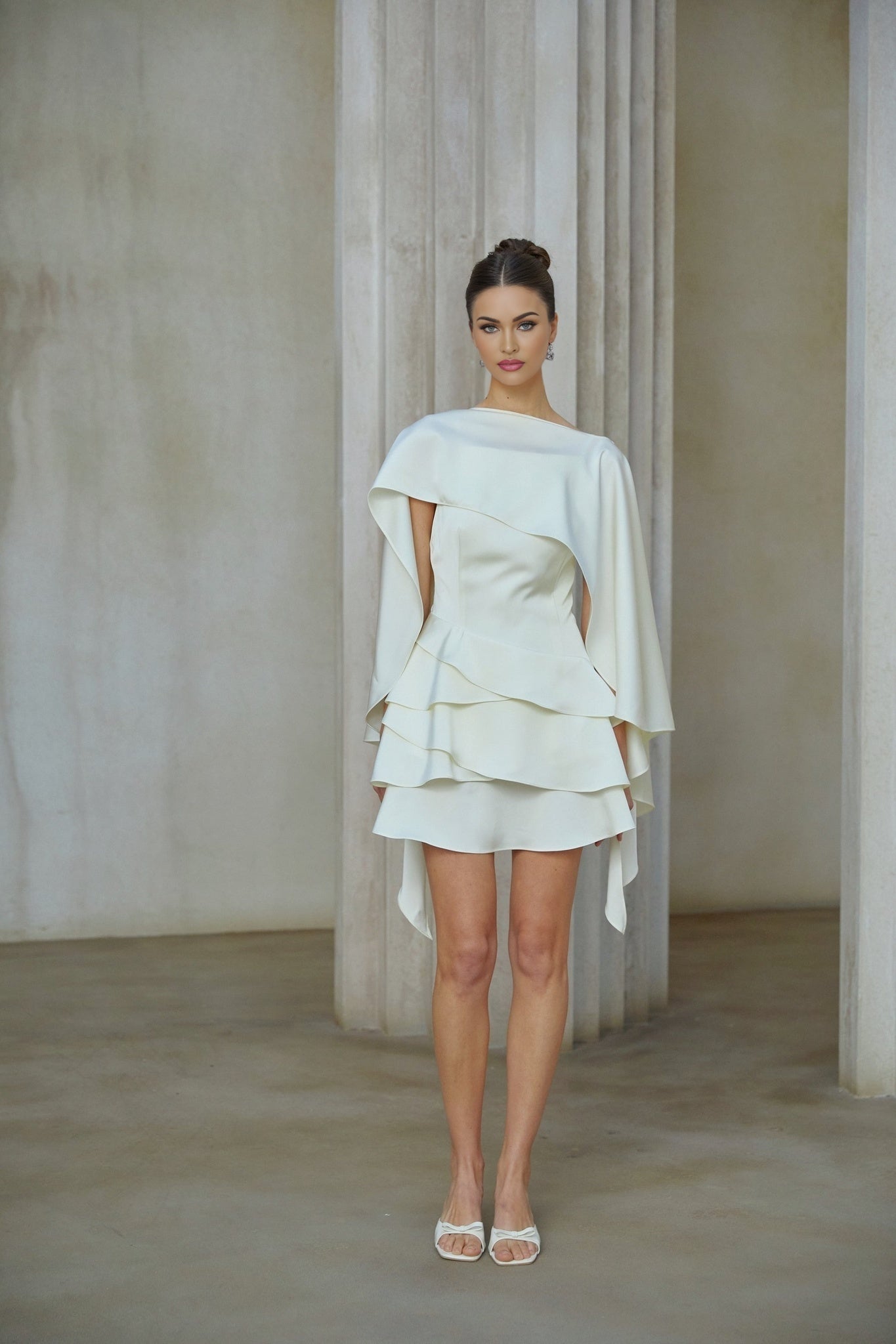 A white satin mini dress with ruffled details and a shawl panel accessory