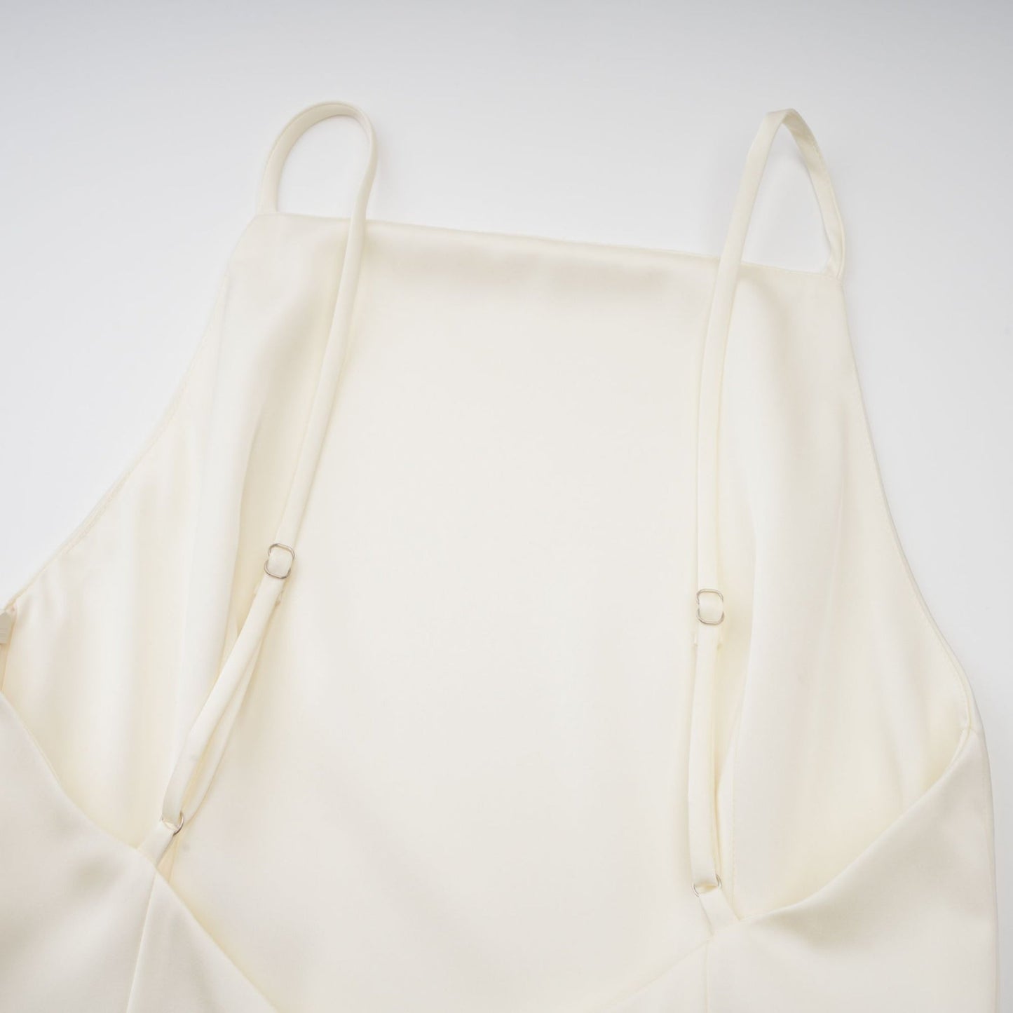 A white satin mini dress with ruffled details and a shawl panel worn by a model against a plain background