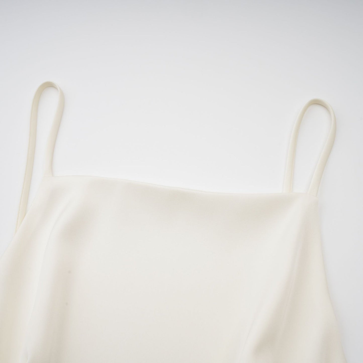 A white satin mini dress with ruffled details and a shawl panel worn by a model against a plain background