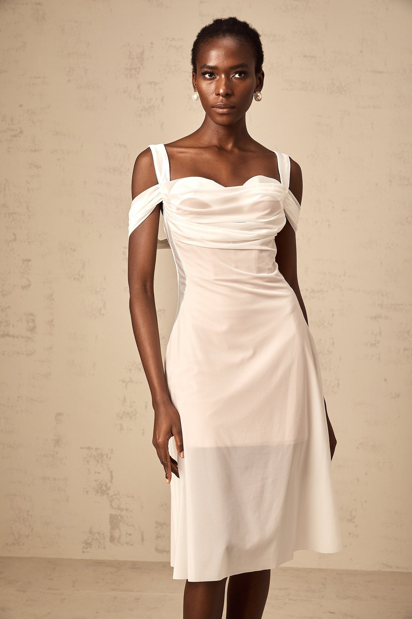 A white semi sheer midi dress with ruched detailing named Gloria worn by a model standing against a plain background