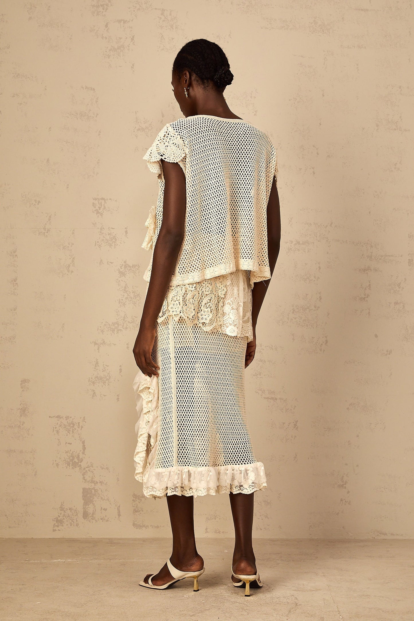 A white sleeveless top with delicate lace panels and crochet knit design featuring a scalloped neckline and intricate floral patterns