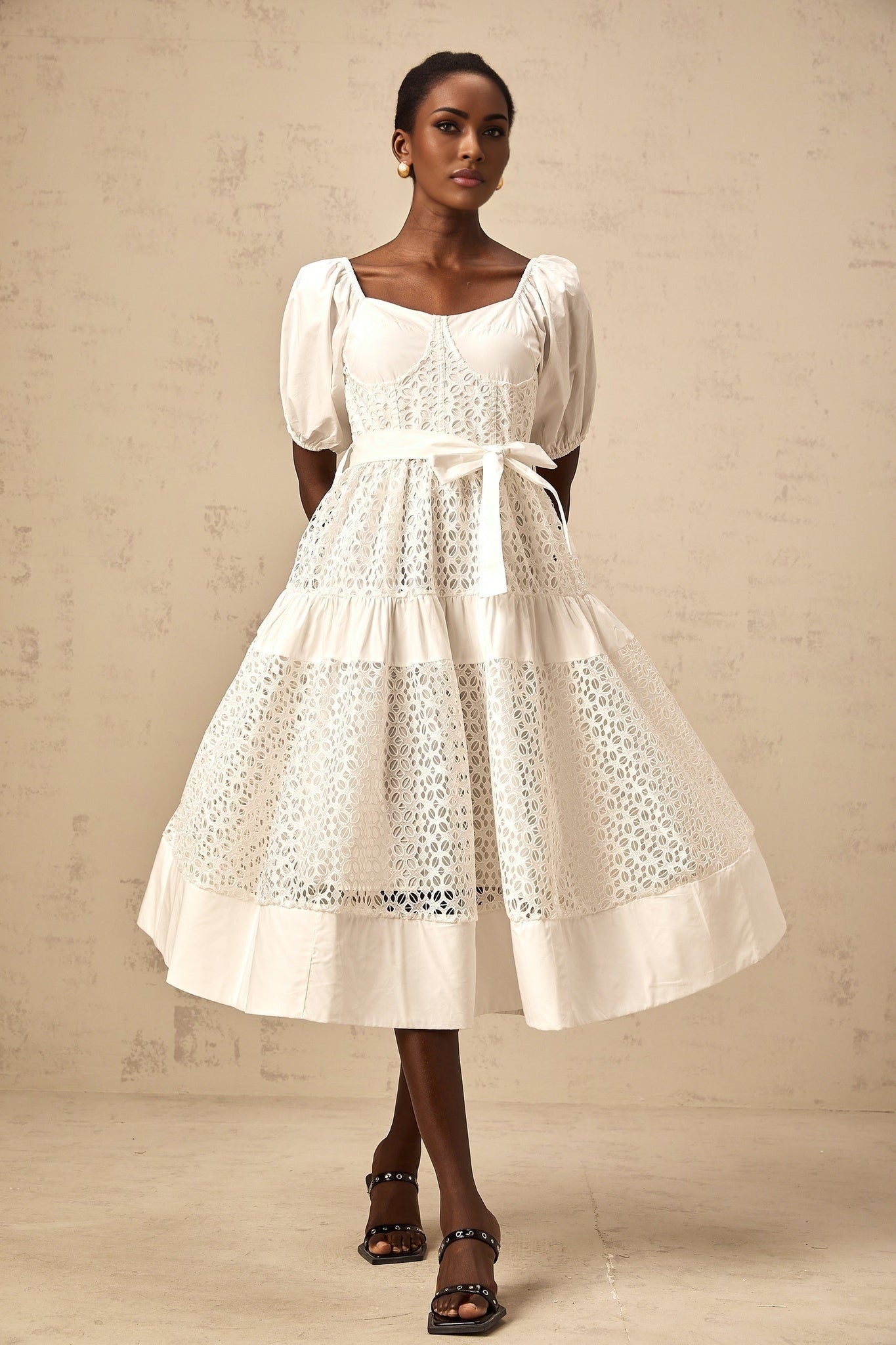 A white tiered midi dress made of corded lace featuring a delicate floral pattern and feminine silhouette