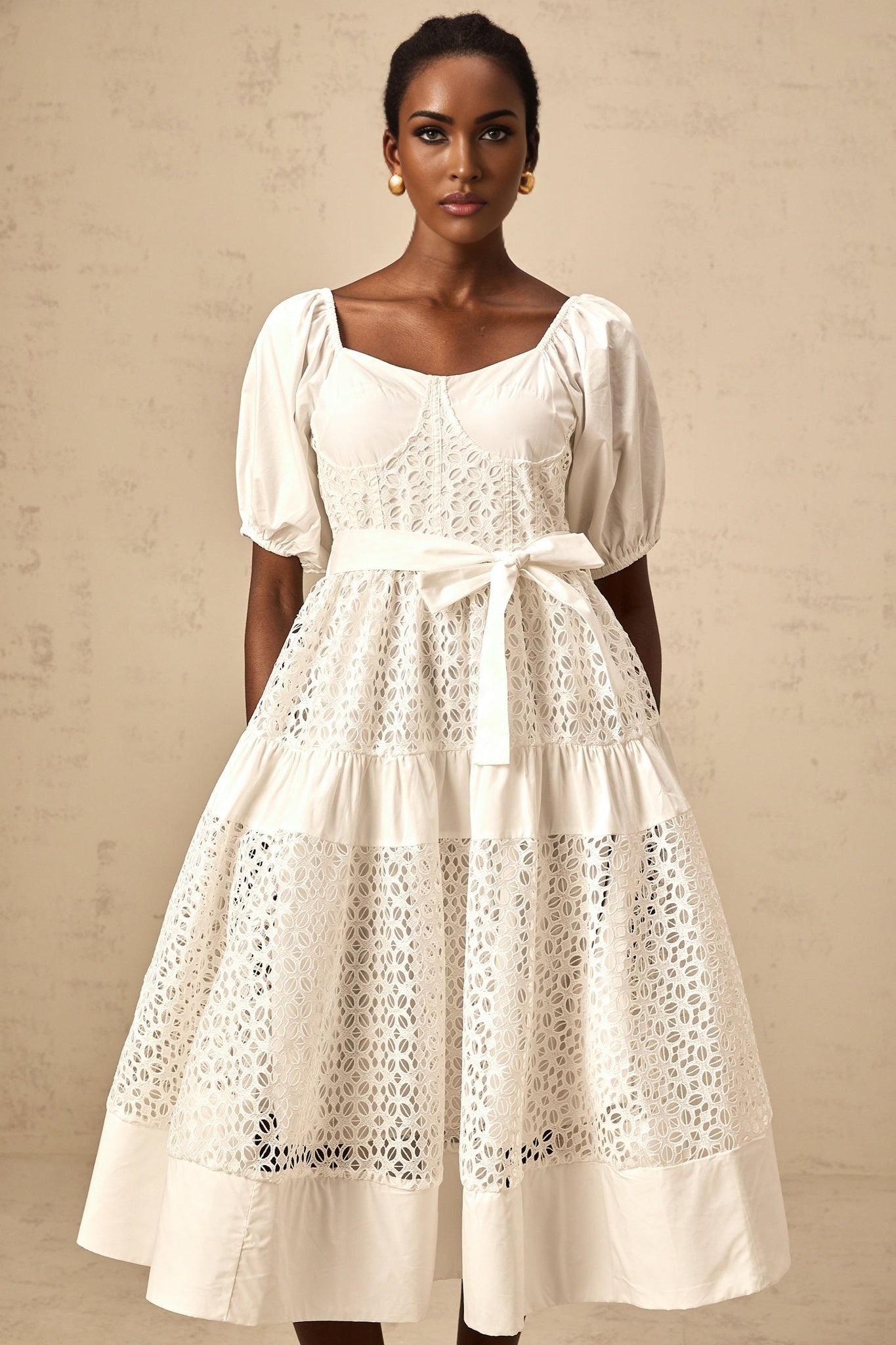 A white tiered midi dress made of corded lace featuring a feminine and delicate design with multiple layers creating a graceful silhouette