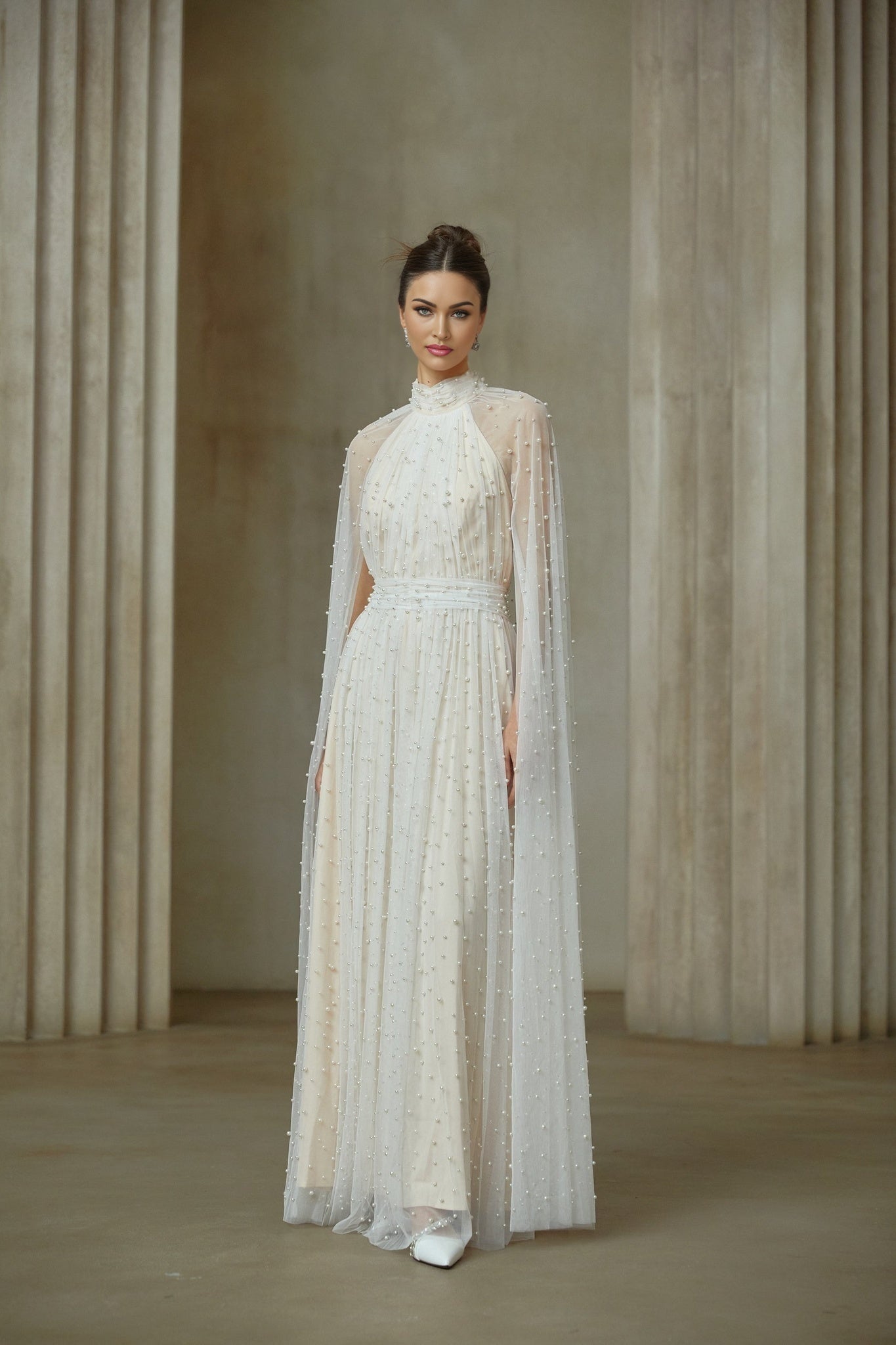 A white tulle maxi dress with cape design and embellishments featuring a flowy silhouette and delicate details