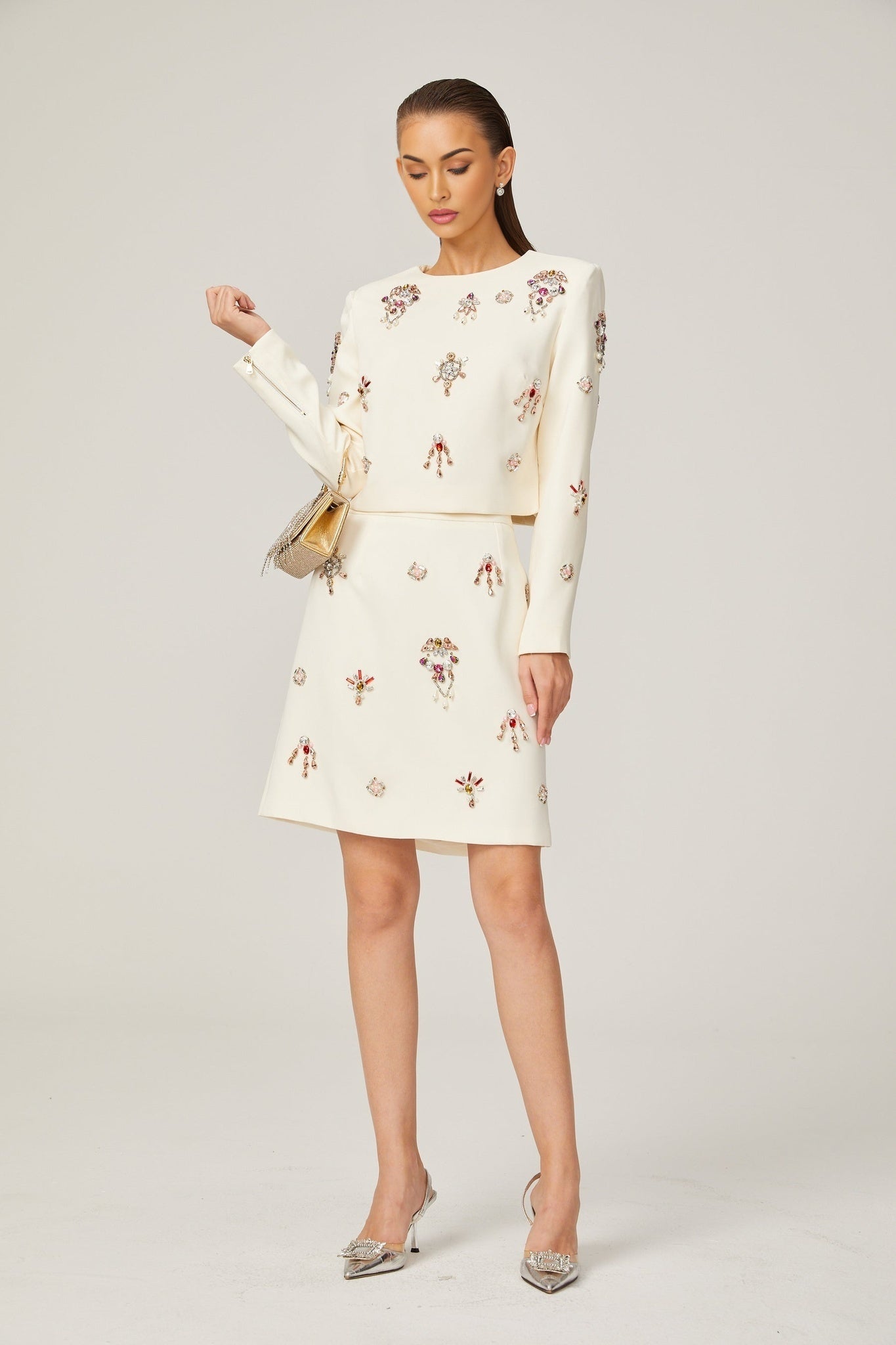 A white twopiece outfit consisting of a top and skirt adorned with crystal embellishments named Jeanne The set features a matching design with sparkling details