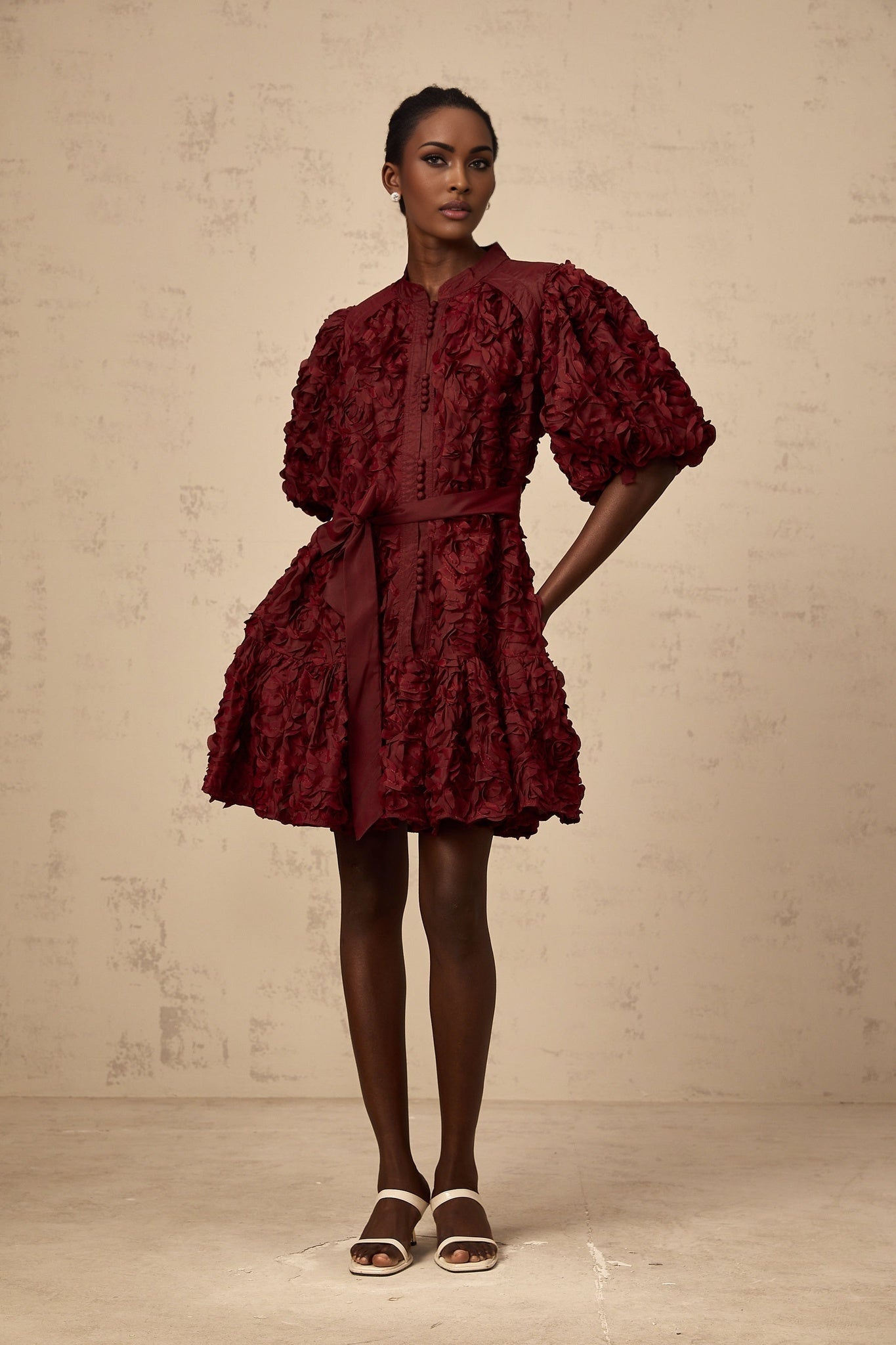 A winered mini dress with a puffed silhouette featuring three dimensional petal details on the fabric