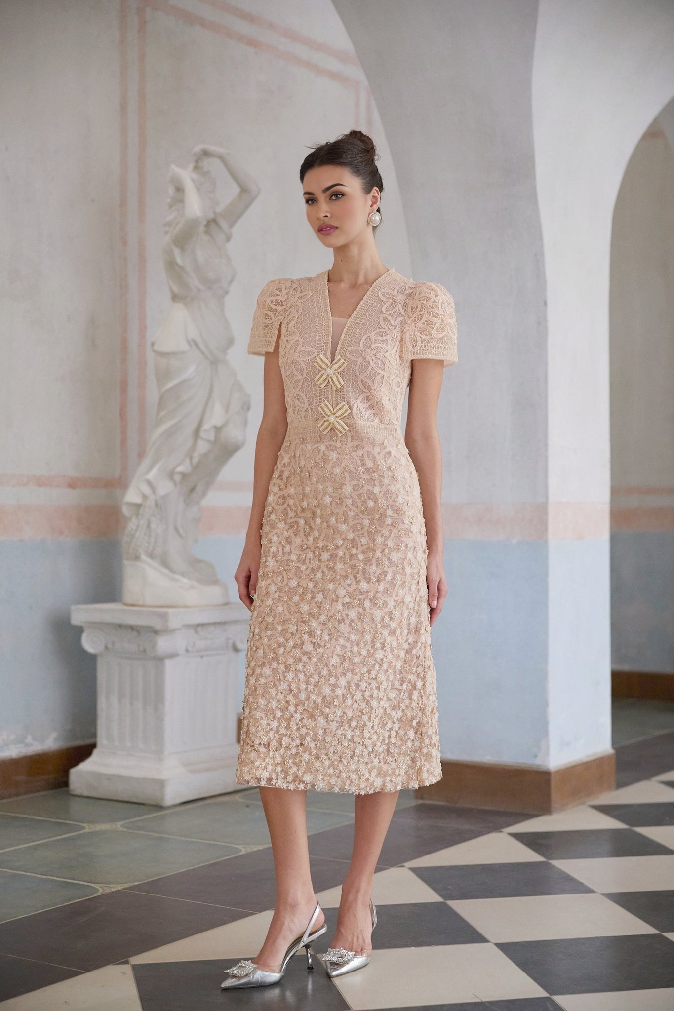 A woman wearing a beige crochet midi dress with a floral pattern and short sleeves standing in a neutral background
