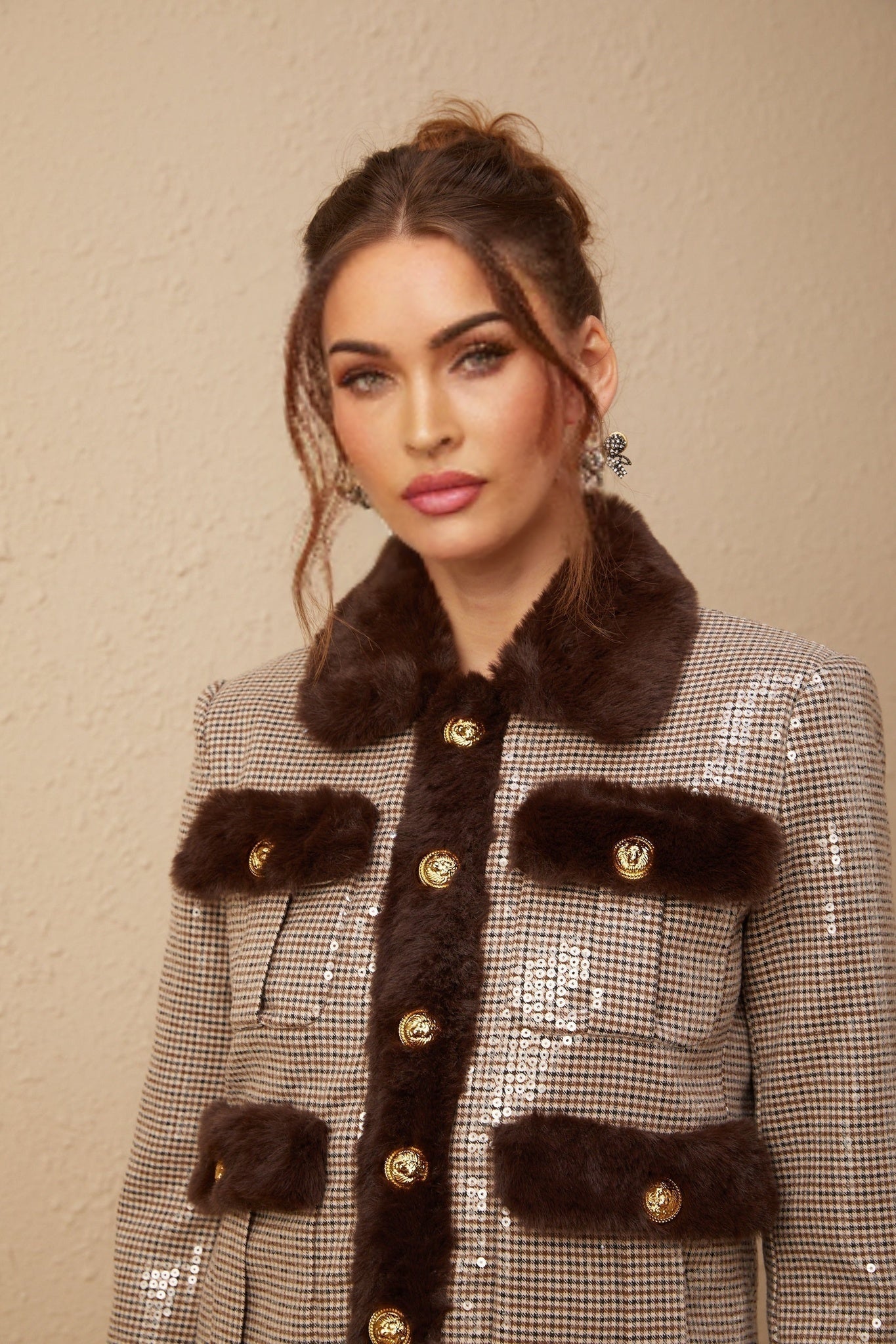 A woman wearing a black and white houndstooth patterned jacket with sequin embellishments and faux fur trim standing against a plain background