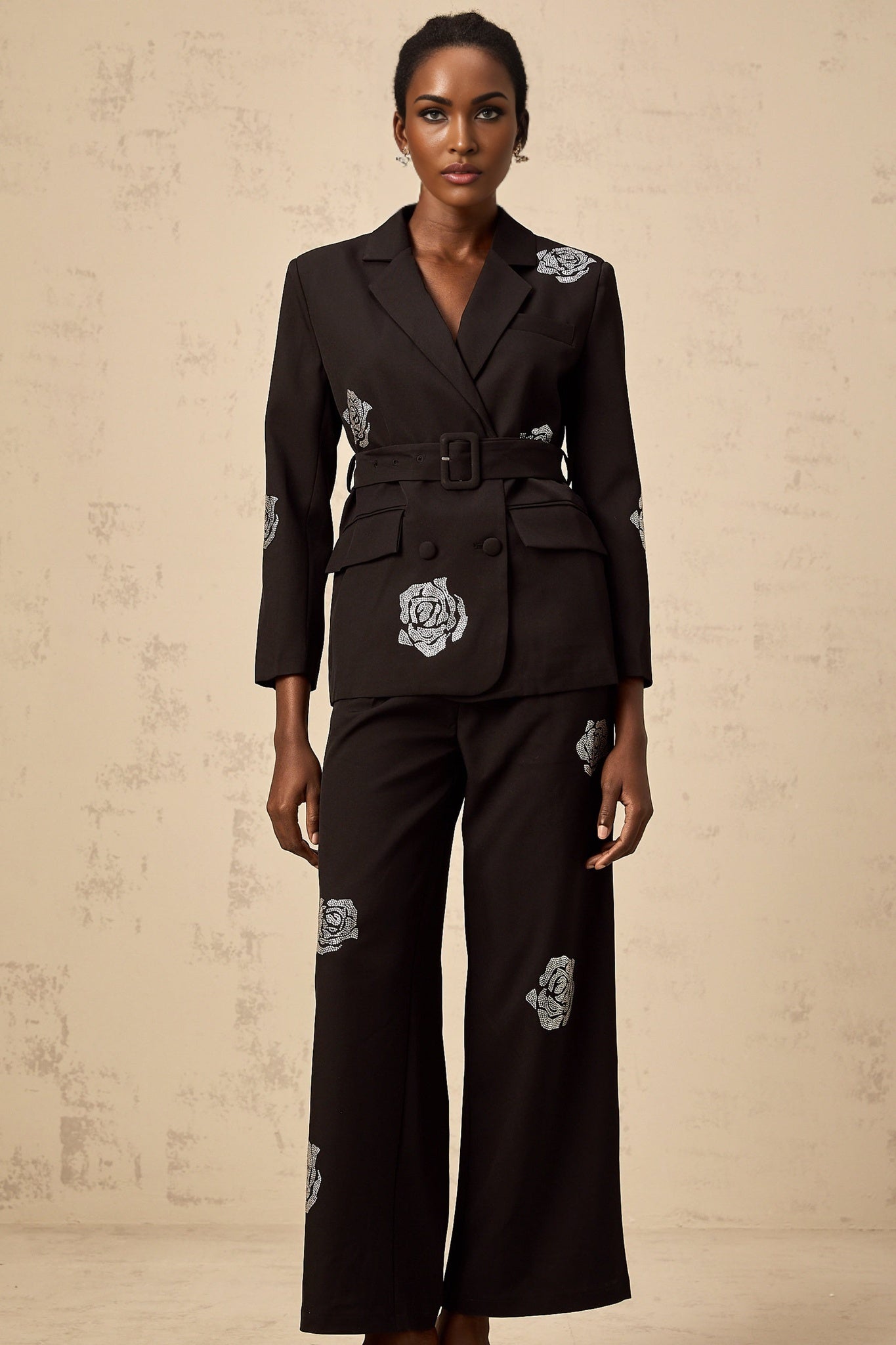 A woman wearing a black blazer and trousers set decorated with studded rose patterns The blazer has a tailored fit and the trousers are slim The outfit is styled as a matching set