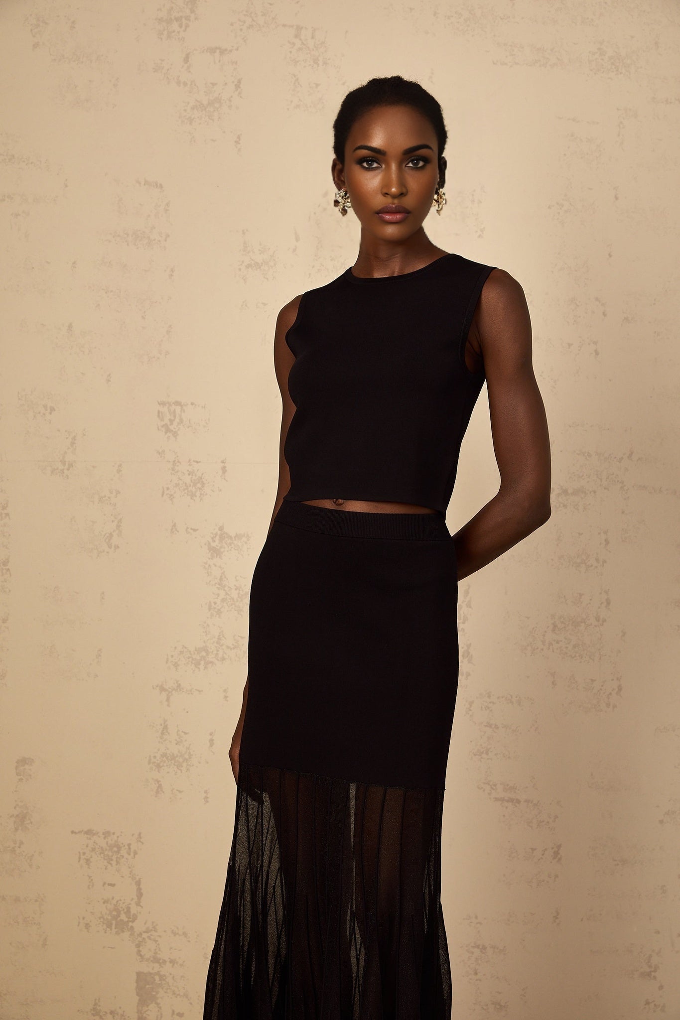 A woman wearing a black fine knit matching set consisting of a top and bottoms with panelled design details