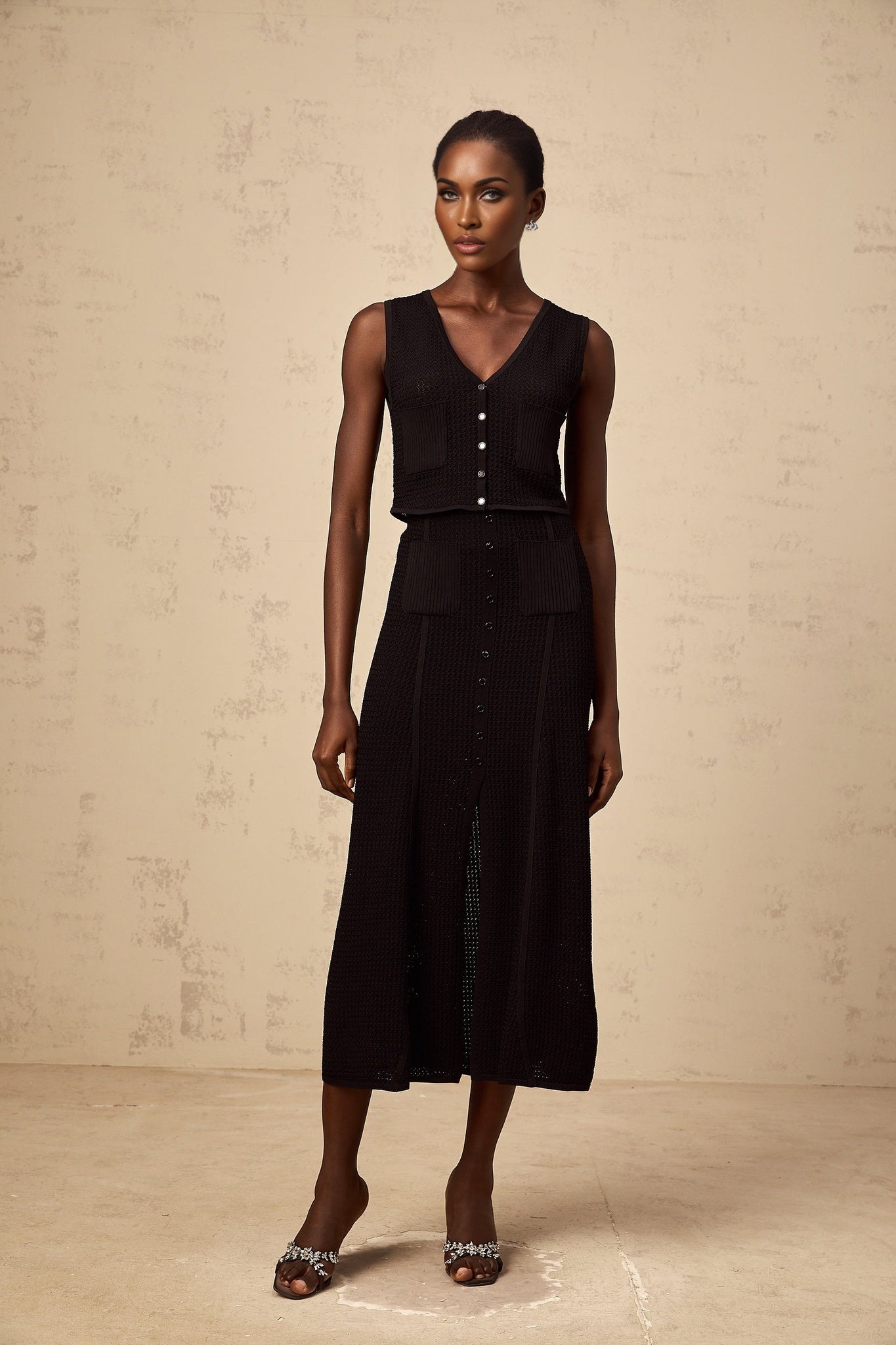 A woman wearing a black matching set consisting of a pointelleknit top and skirt The top has short sleeves and the skirt falls to mid thigh Both pieces feature delicate knit patterns throughout