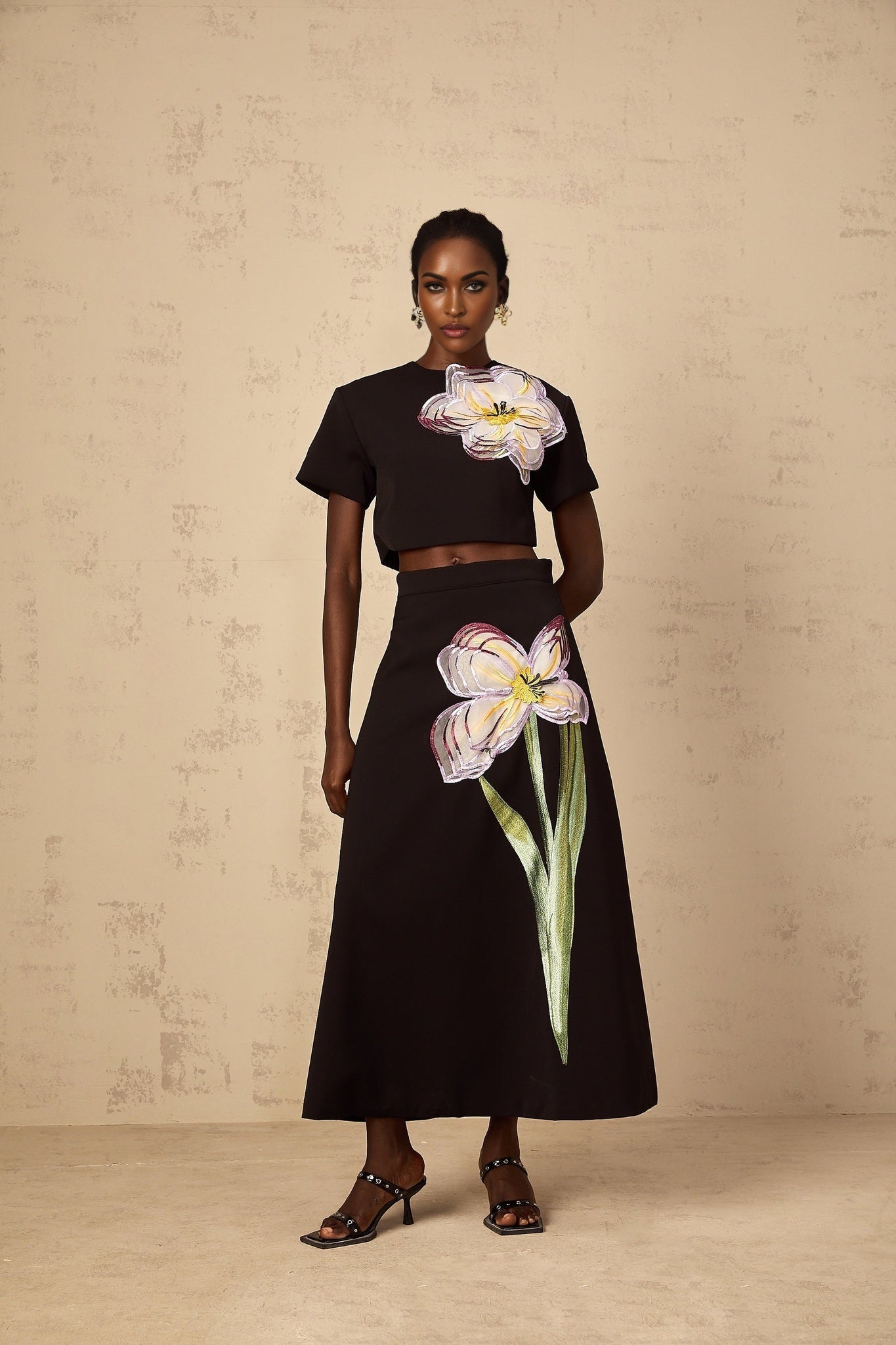 A woman wearing a black matching set featuring sequin floral embroidery on both the top and bottom pieces