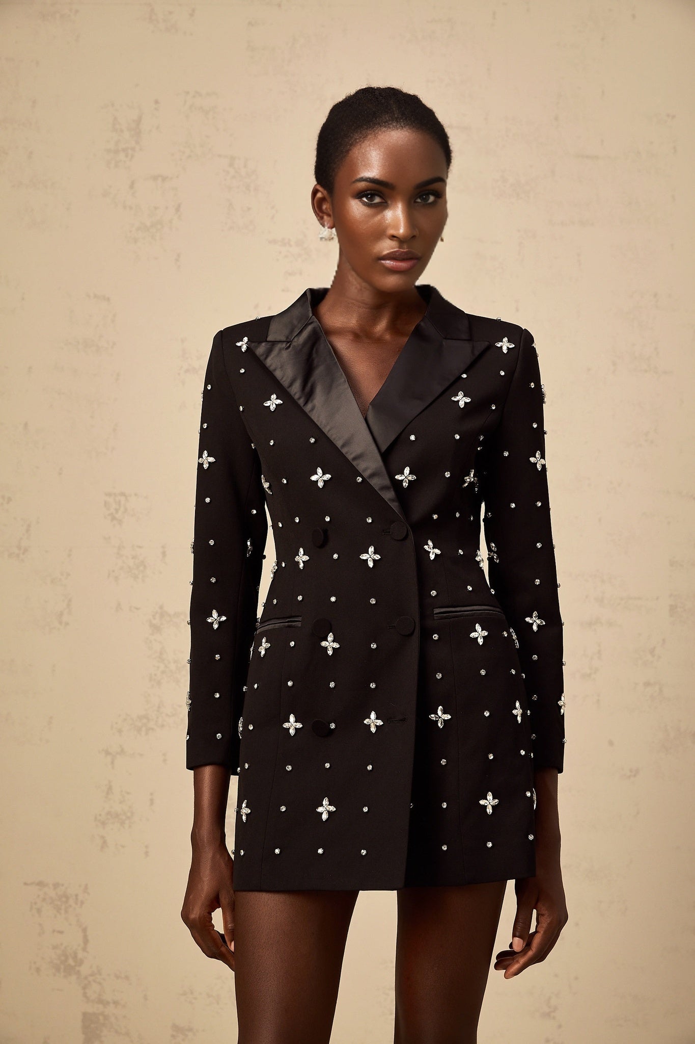 A woman wearing a black mini blazer dress with crystal embellishments and panelled details standing in a stylish pose