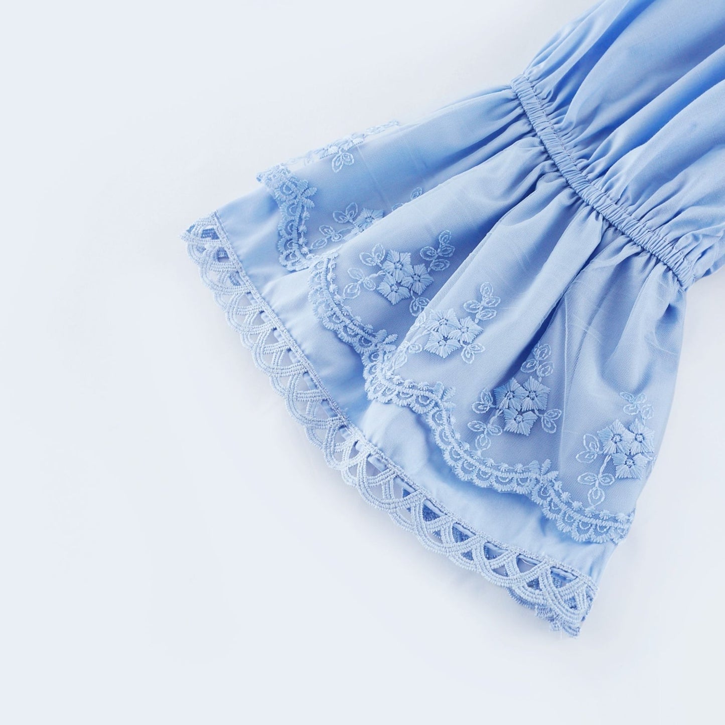 A woman wearing a black offshoulder tiered midi dress with flowy layers standing against a plain background