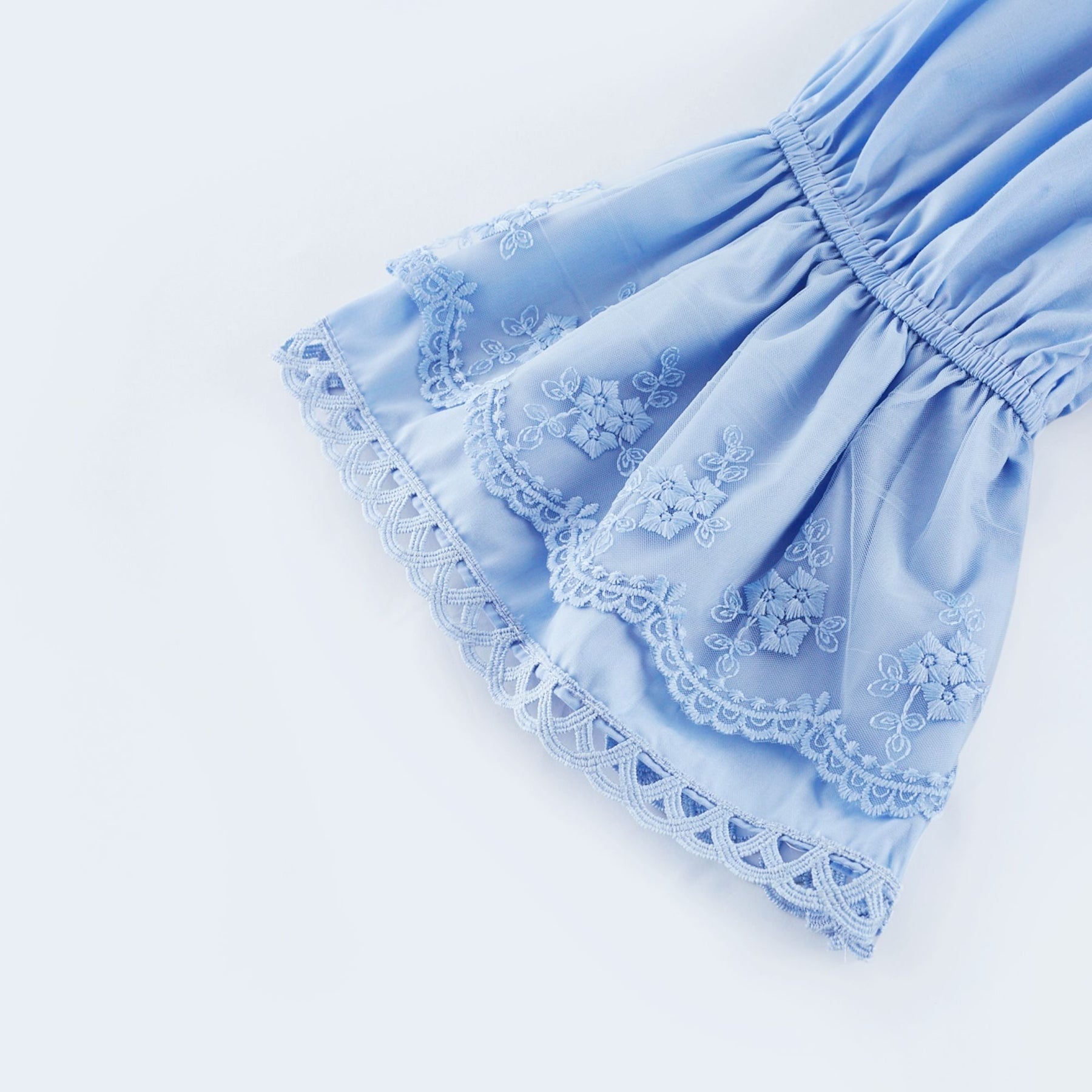 A woman wearing a black offshoulder tiered midi dress with flowy layers standing against a plain background