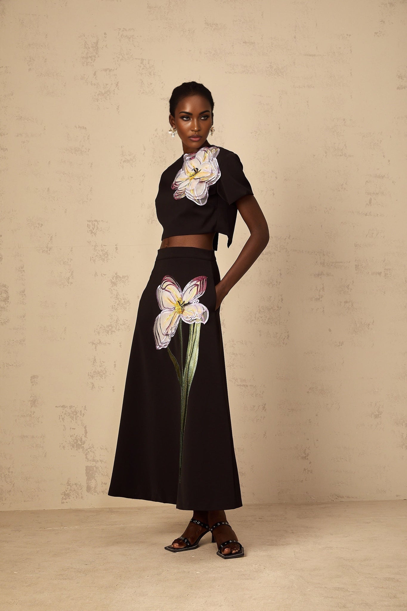 A woman wearing a black sequin matching set with floral embroidery featuring a crop top and high waisted pants