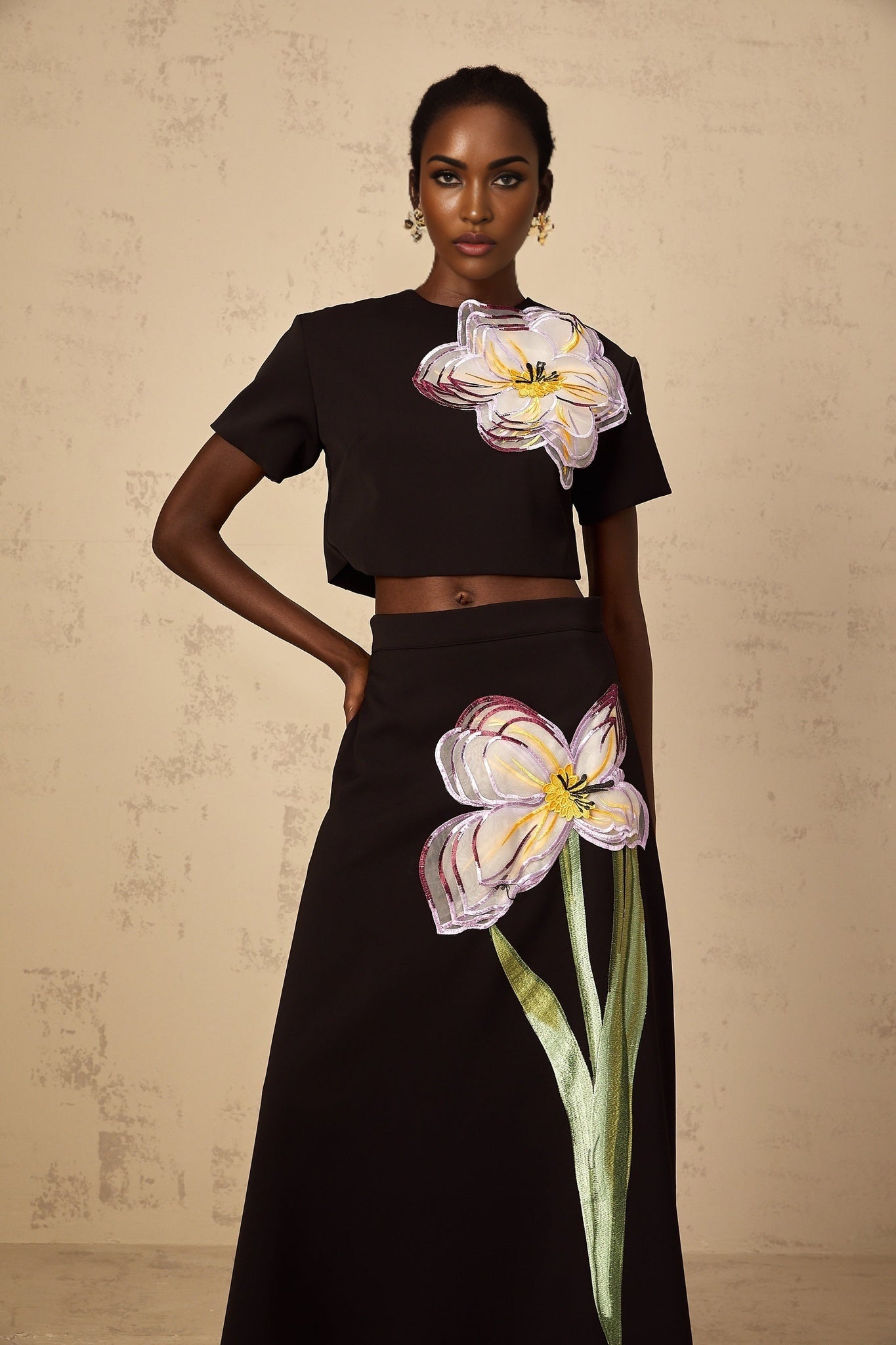 A woman wearing a black two piece outfit with sequin floral embroidery consisting of a cropped top and matching bottoms