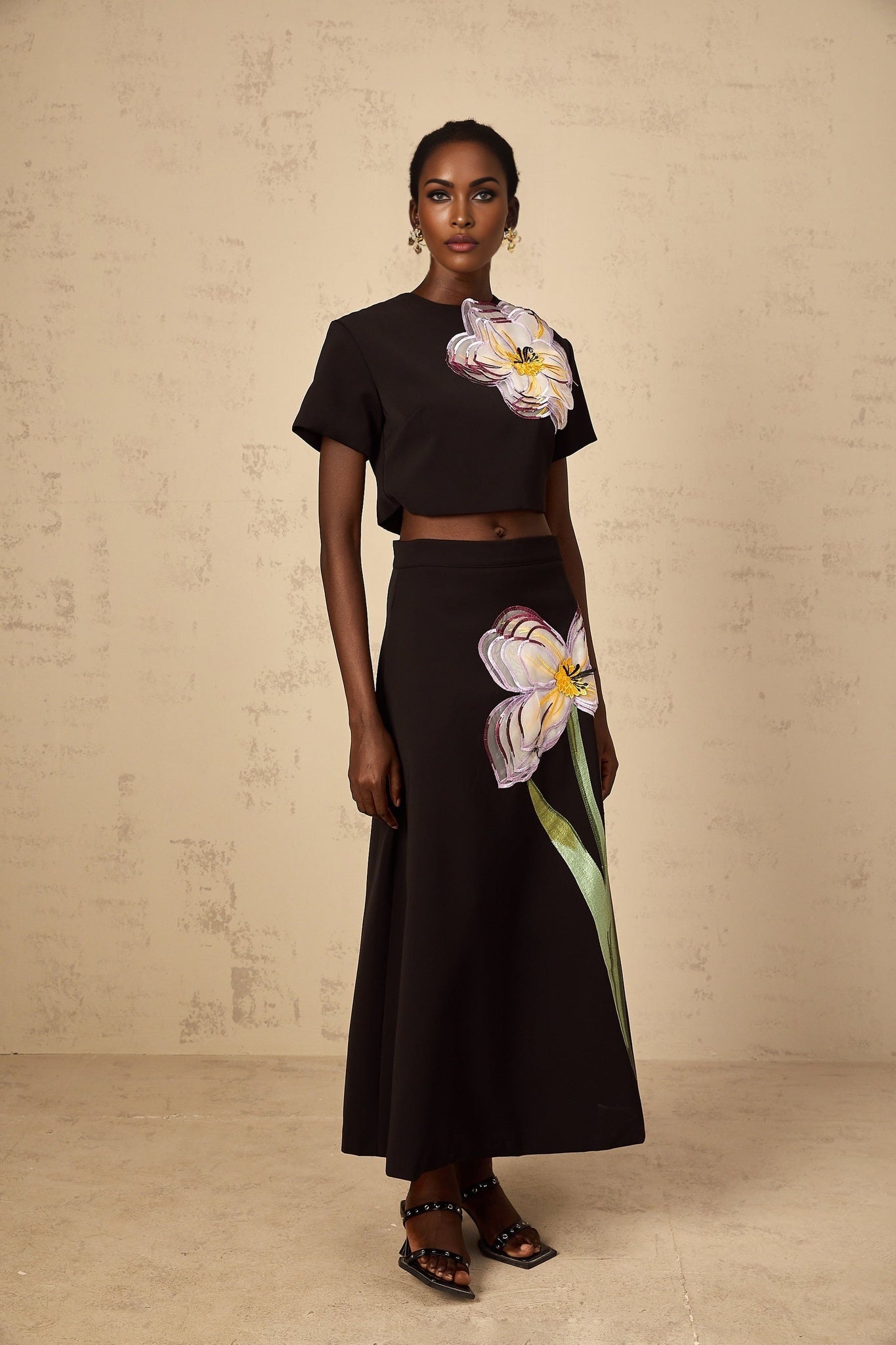 A woman wearing a black twopiece outfit featuring sequin floral embroidery on both the top and bottom pieces of the matching set