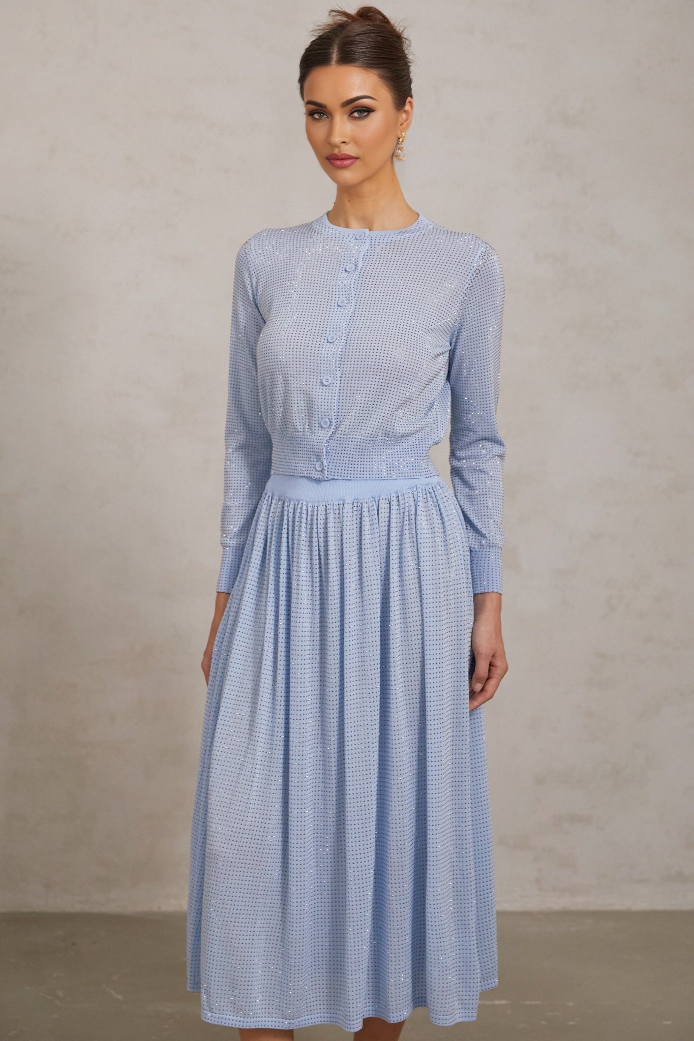 A woman wearing a blue knitted two piece outfit consisting of a sleeveless top and skirt adorned with sparkling rhinestones The set has a fitted silhouette and shimmering texture