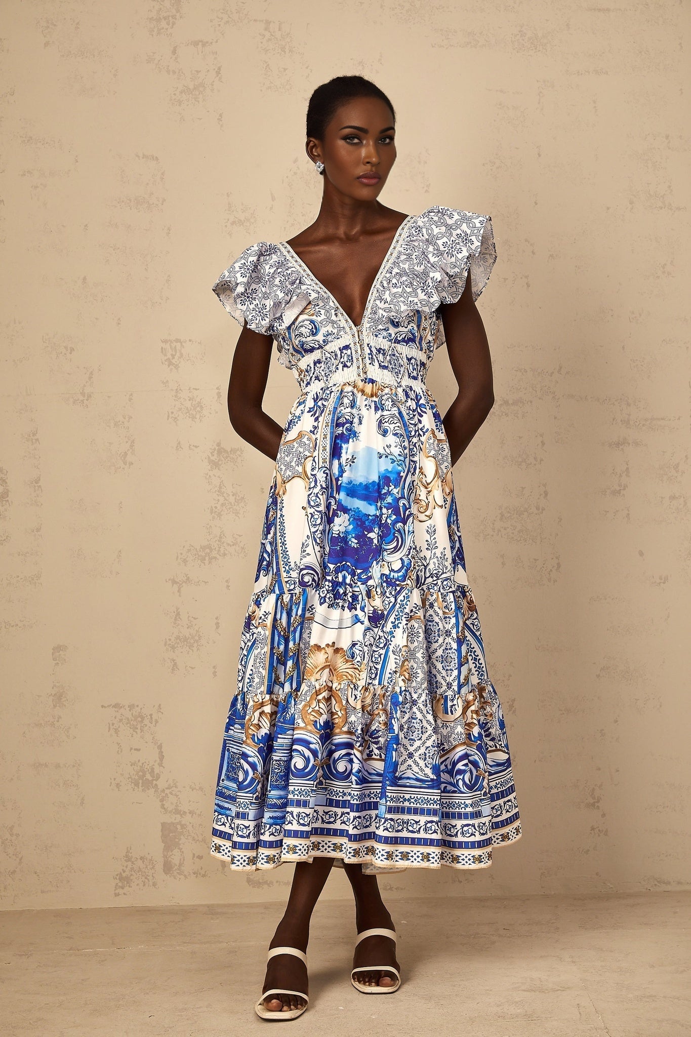 A woman wearing a blue midi dress with a baroque print pattern and tiered skirt design