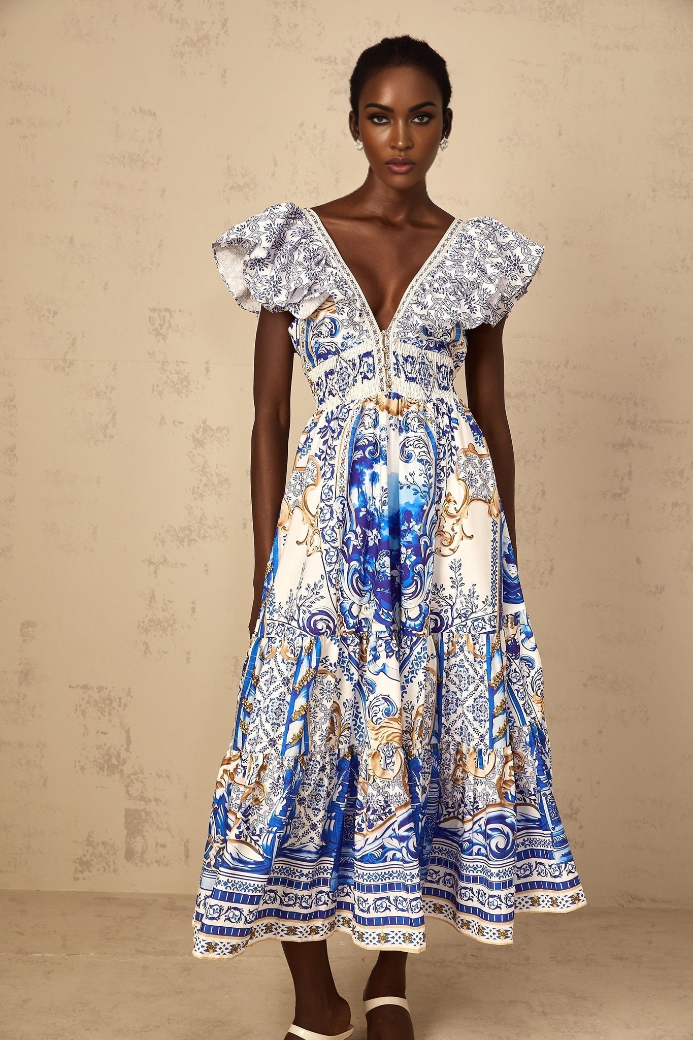 A woman wearing a blue midi dress with a baroque print pattern and tiered skirt design