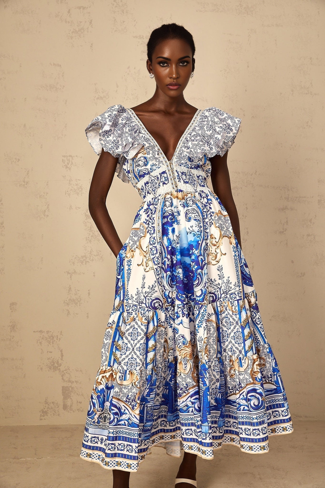 A woman wearing a blue midi dress with a baroque print pattern and tiered skirt design