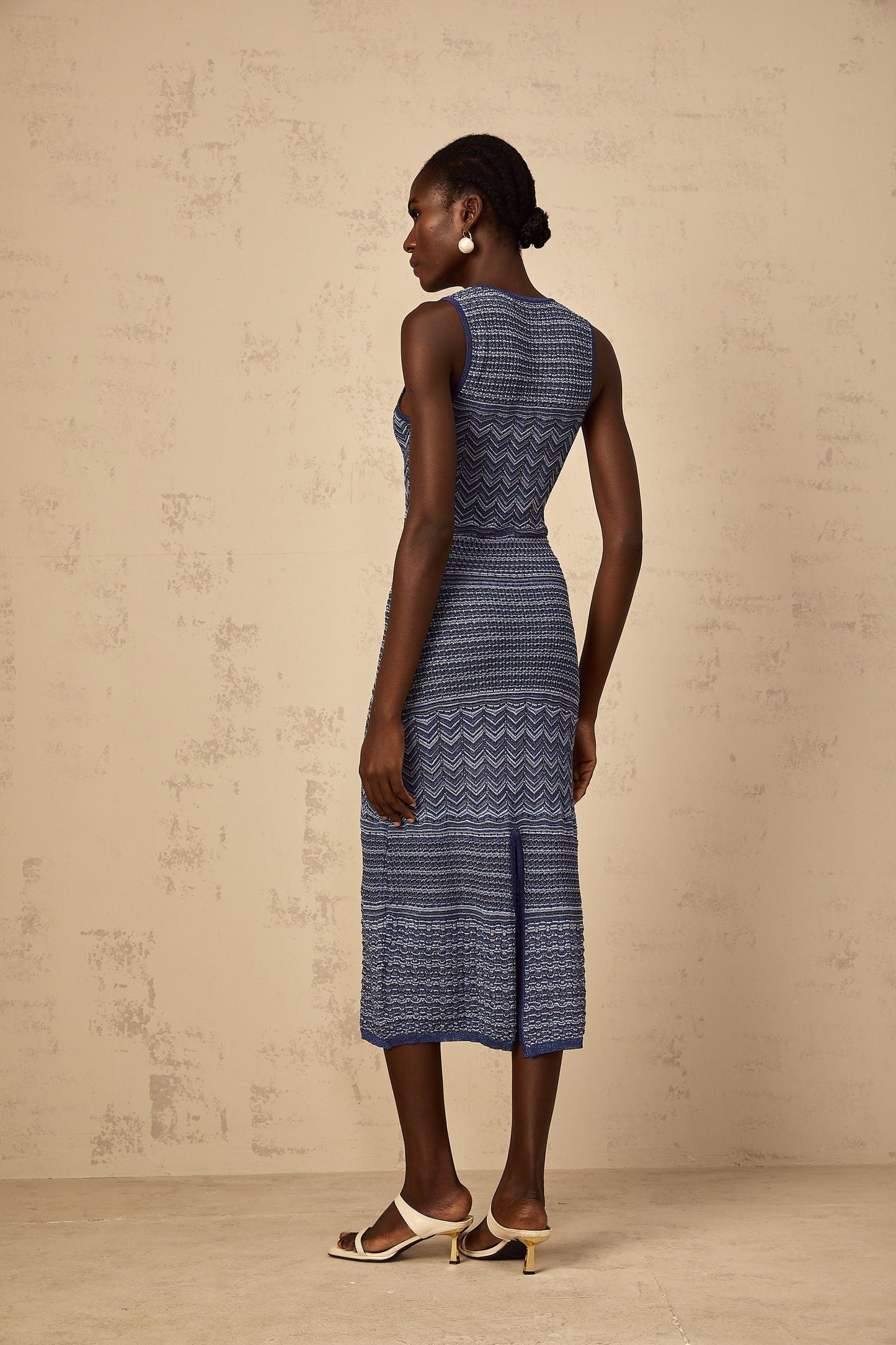 A woman wearing a blue midi dress with a wavy crochet knit pattern standing in a relaxed pose