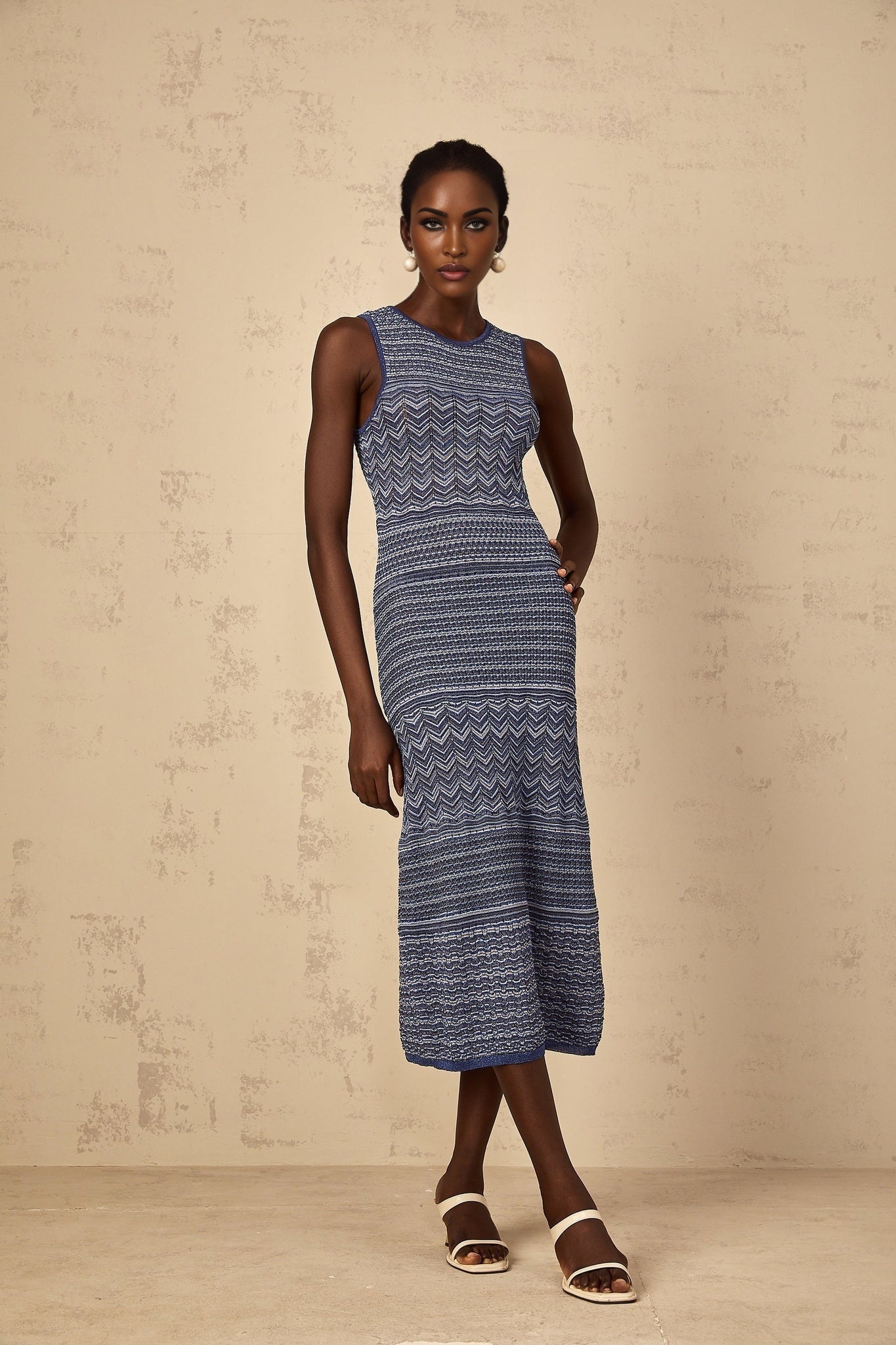 A woman wearing a blue midi dress with a wavy crochet knit pattern standing in a relaxed pose