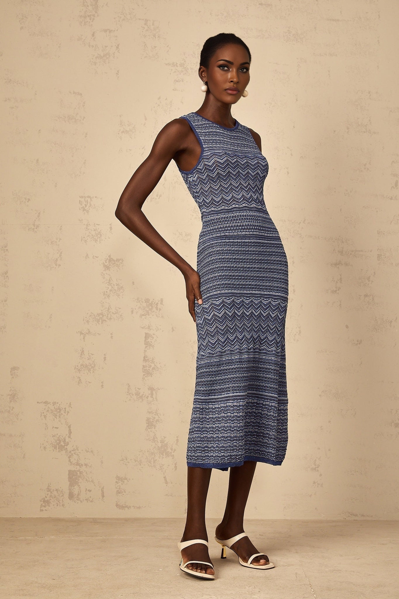 A woman wearing a blue midi dress with a wavy crochet knit pattern standing in a relaxed pose