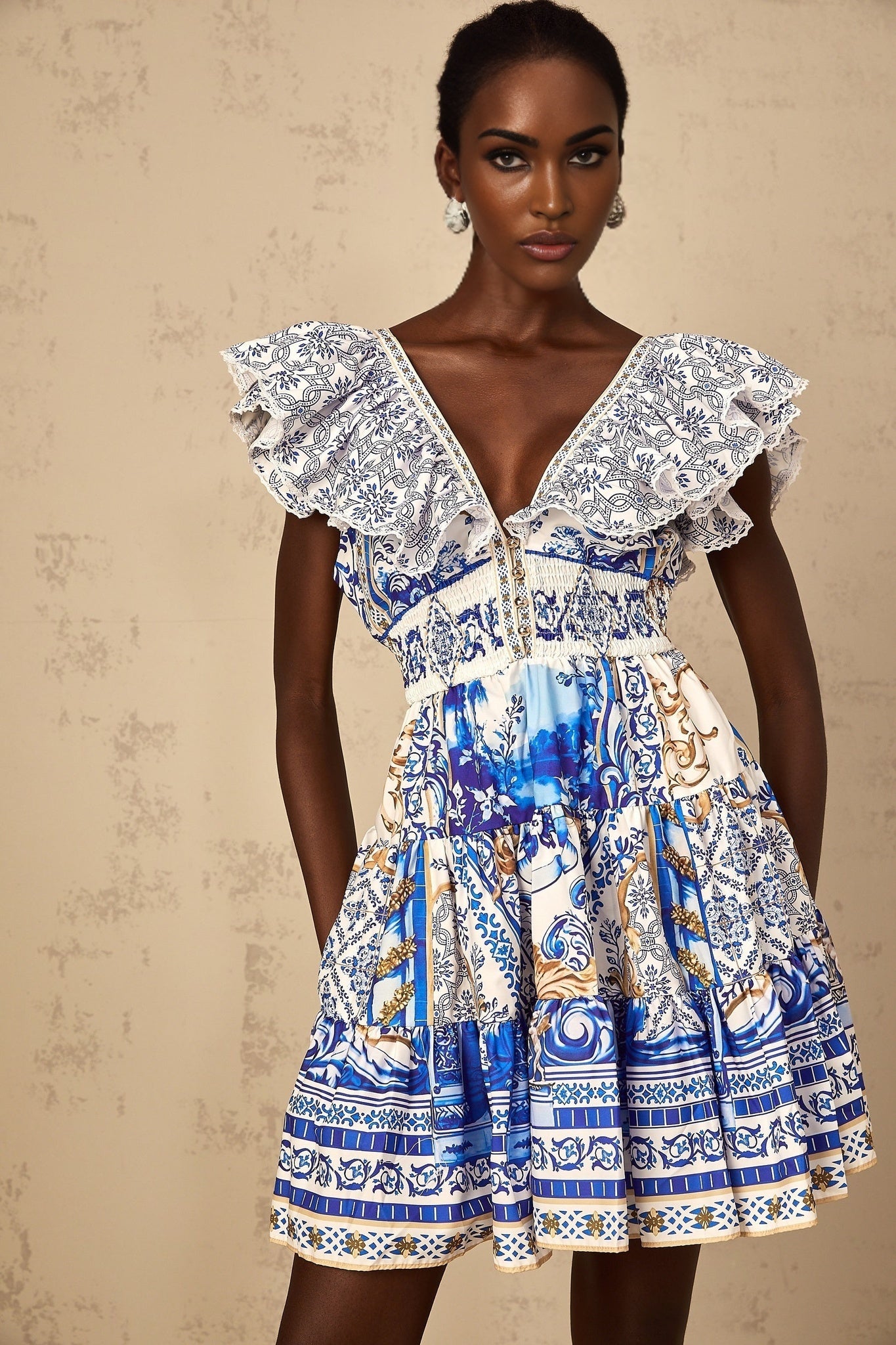 A woman wearing a blue mini dress with a baroque print pattern and tiered skirt design