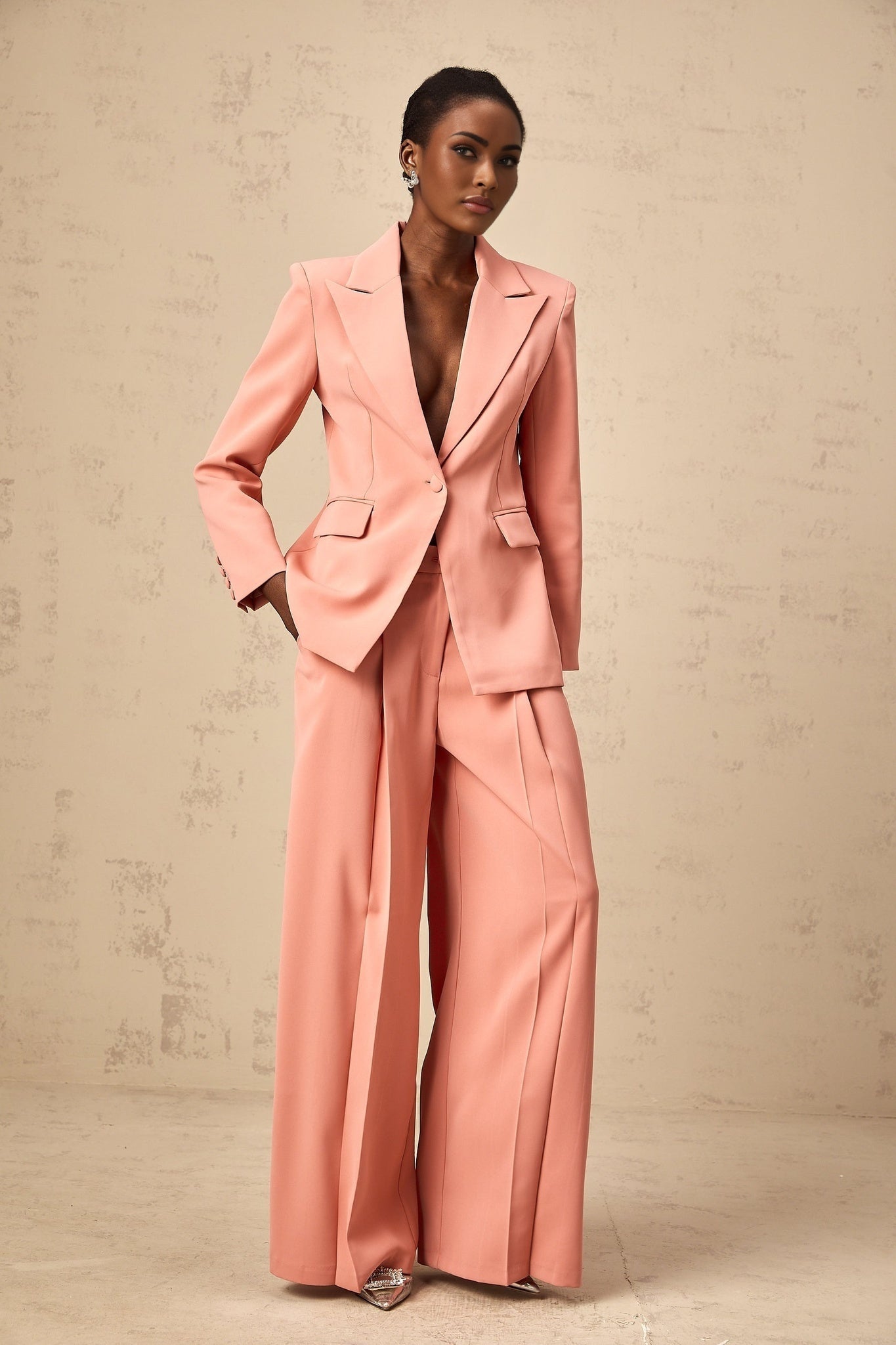 A woman wearing a bright pink matching set consisting of a blazer with cutout details and embroidery paired with coordinating trousers