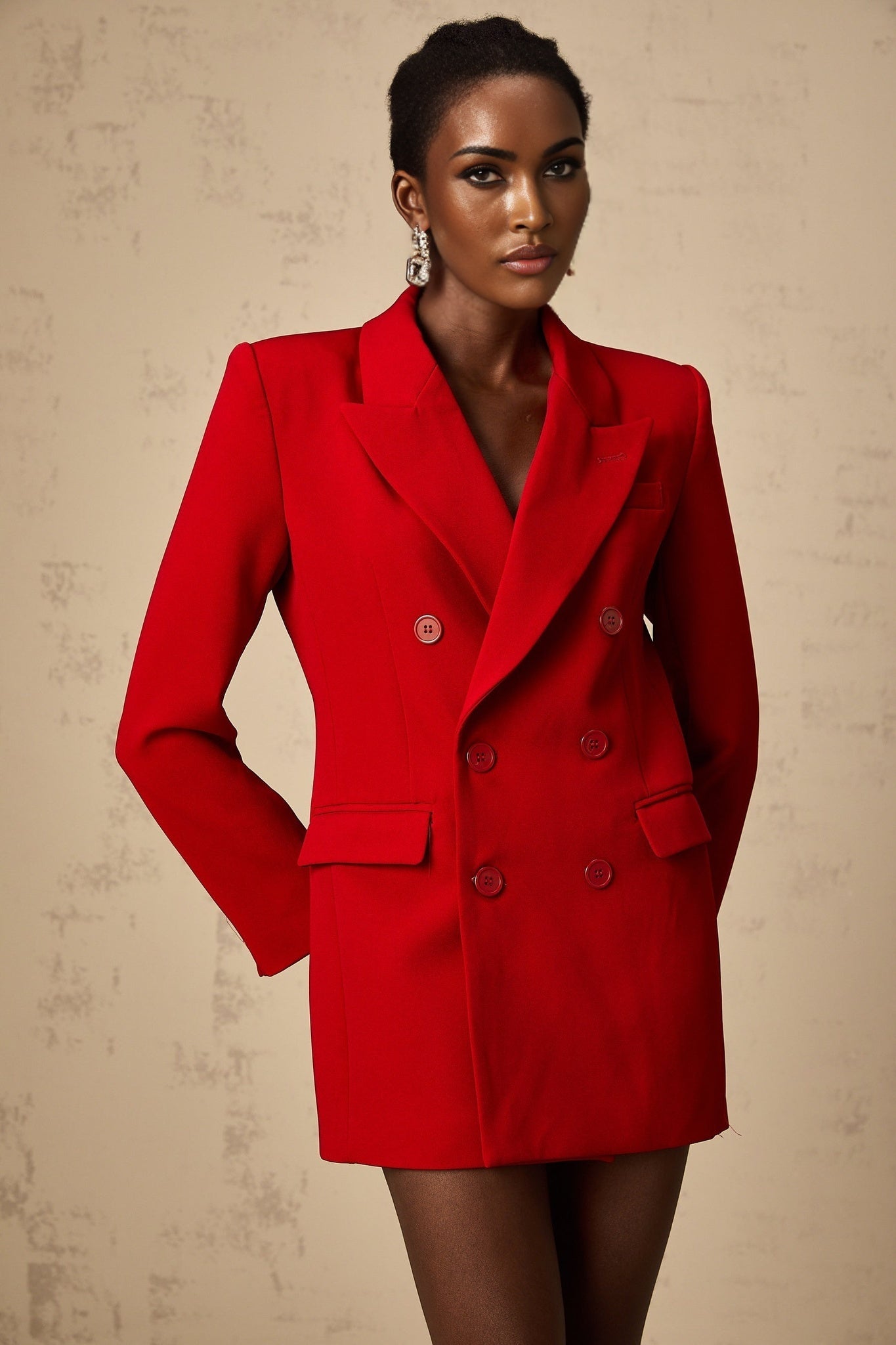 A woman wearing a bright red doublebreasted blazer with lapels and buttons visible against a plain background