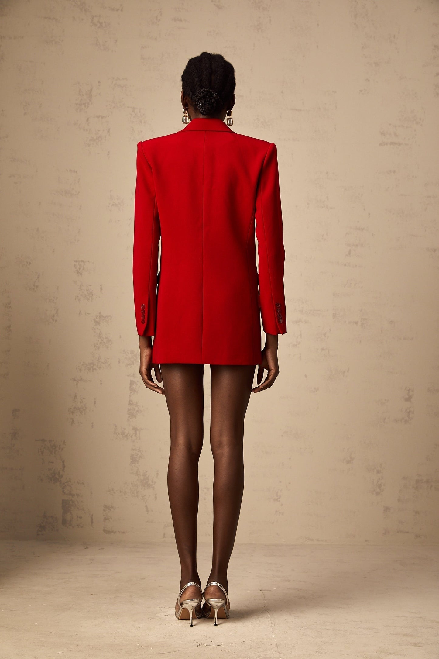 A woman wearing a bright red doublebreasted blazer with lapels and buttons visible against a plain background