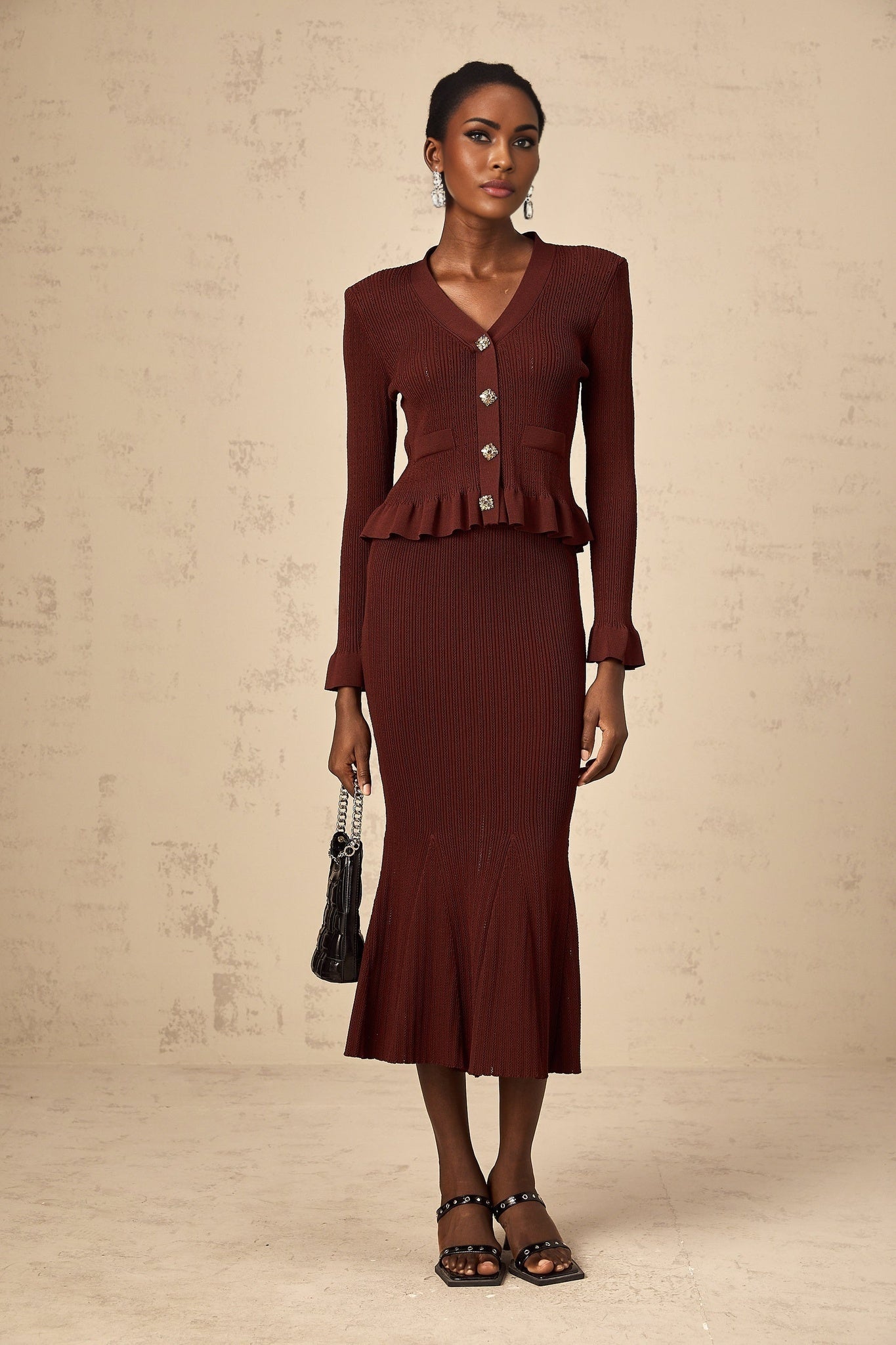 A woman wearing a bright red matching set consisting of a ruffled knit top and skirt The top features a sleeveless design with ruffle details while the skirt has a fitted silhouette Both pieces are made from a textured knit fabric creating a coordinated and stylish outfit