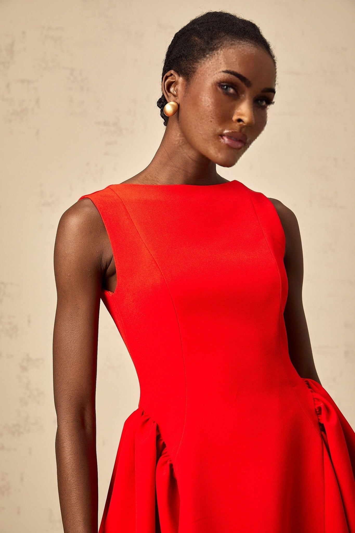 A woman wearing a bright red sleeveless mini dress with a flared skirt standing against a plain background