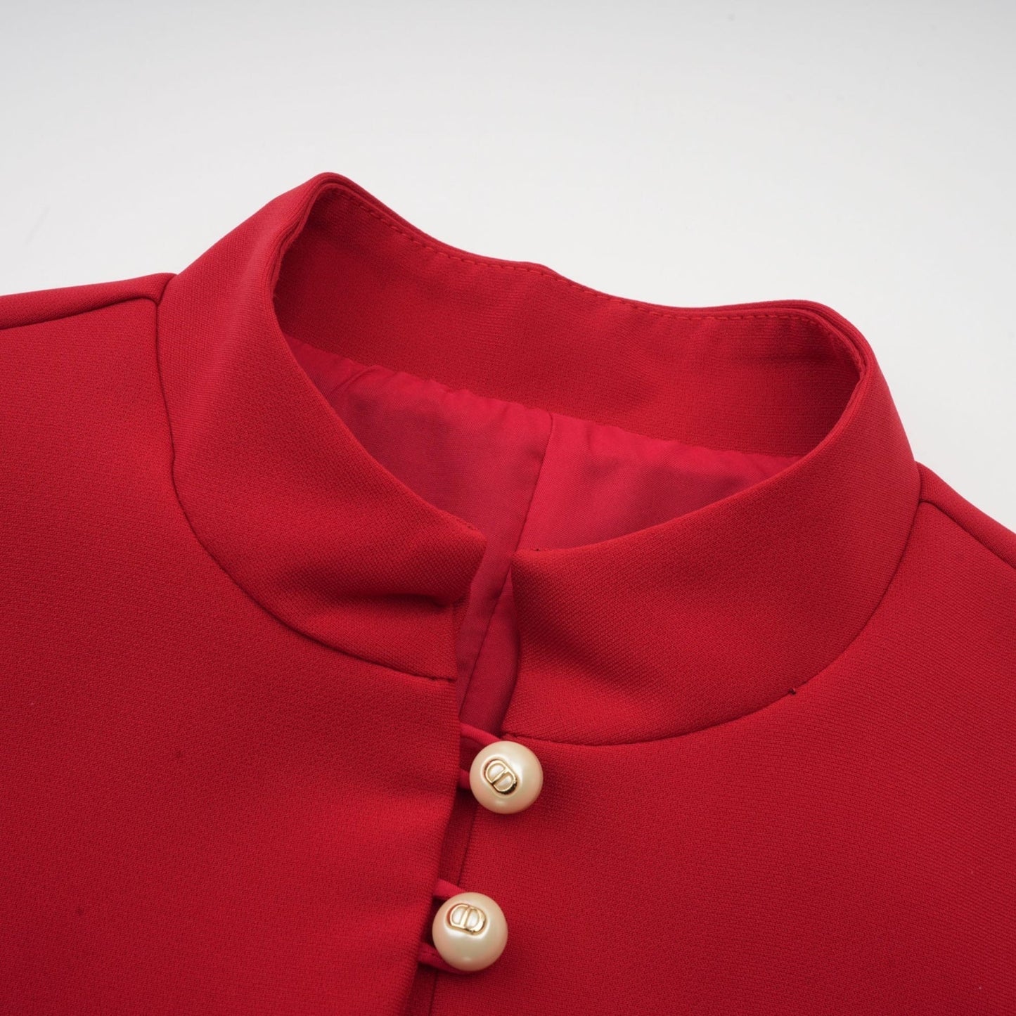 A woman wearing a bright red twopiece outfit consisting of a pleated blouse and matching pleated skirt standing against a plain background